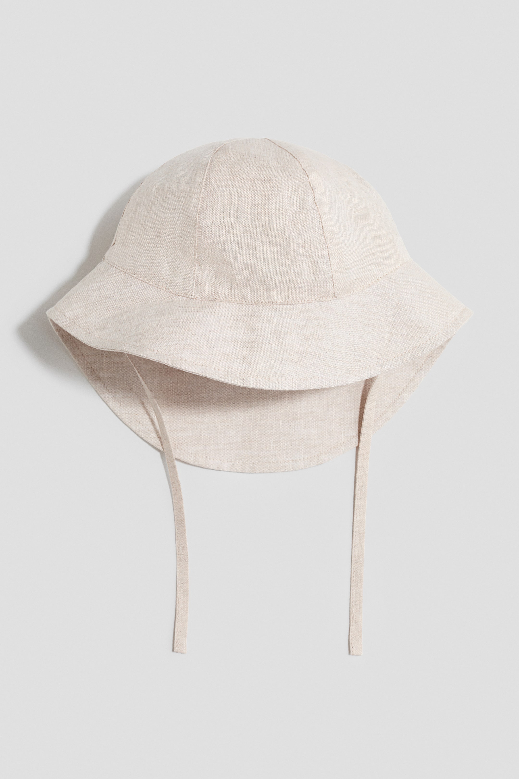 Ver imagen más grande: Un sombrero de sol se presenta de FRENTE, confeccionado en lino beige claro con una corona panelada. Cuenta con un ala ancha que es visiblemente más larga en la parte trasera, y dos finas cintas de tela cuelgan de cada lado.