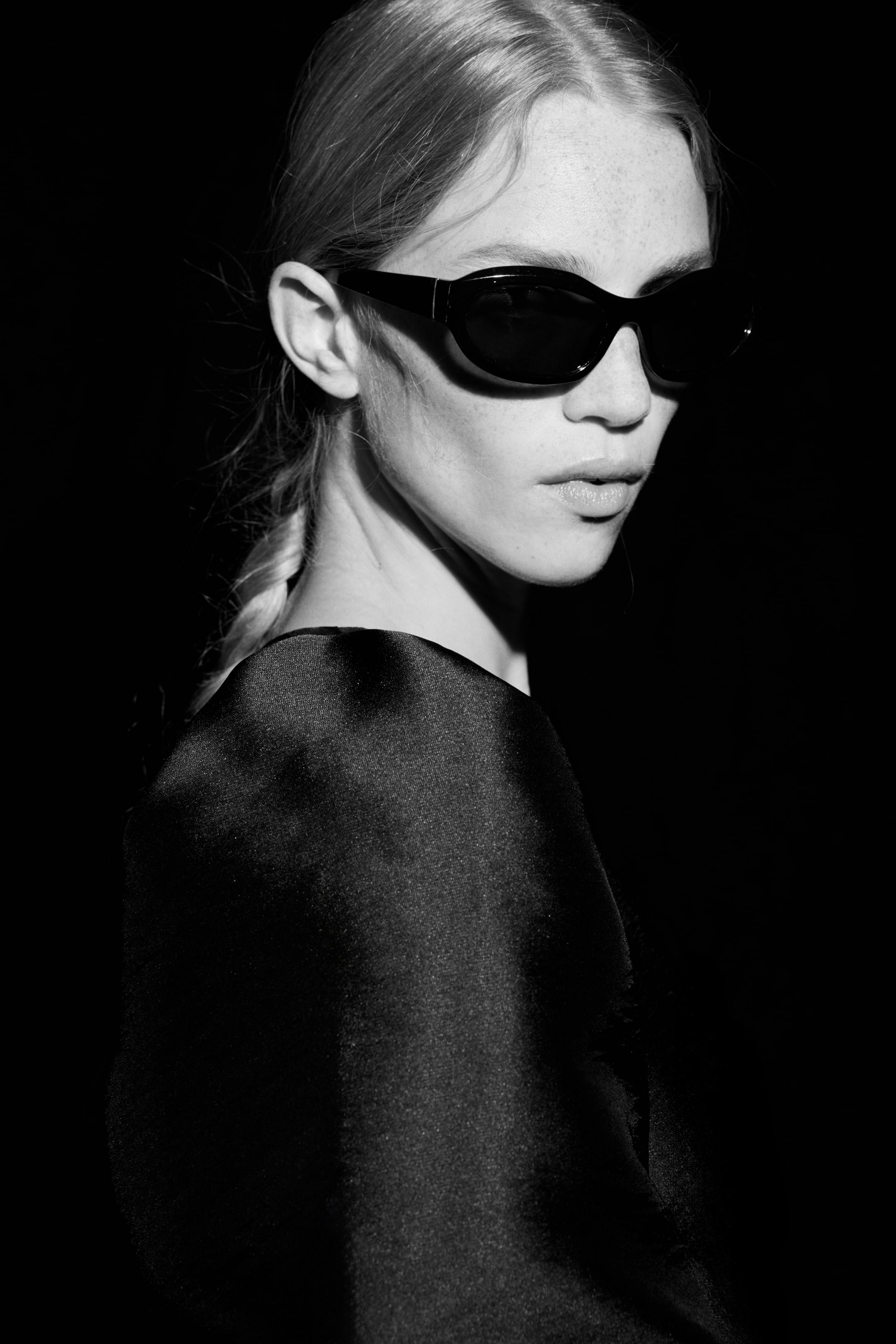 View larger image: Black sunglasses are being worn, featuring thick, dark frames and opaque lenses. The frames are presenting an elongated oval shape that curves around the face, visible from a three-quarter profile.