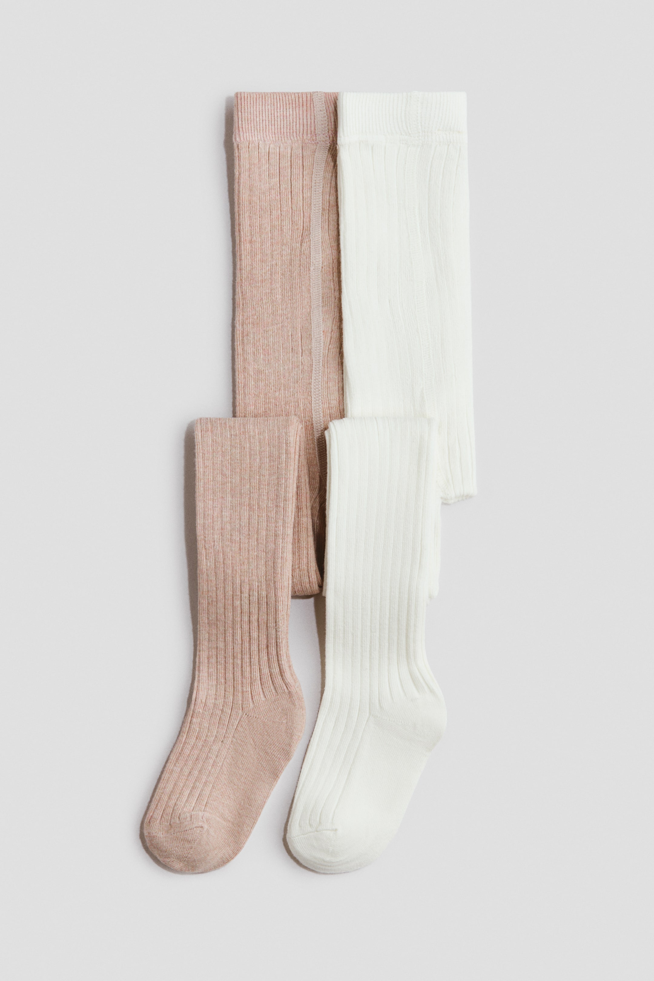 Größeres Bild ansehen: Zwei Paar H&M Adorables Strumpfhosen werden nebeneinander flach ausgelegt präsentiert. Ein Paar ist in einem hellen Rosé-Beige gehalten, das andere in Weiß. Beide zeigen eine markante Rippstrickstruktur und elastische Taillenbänder.