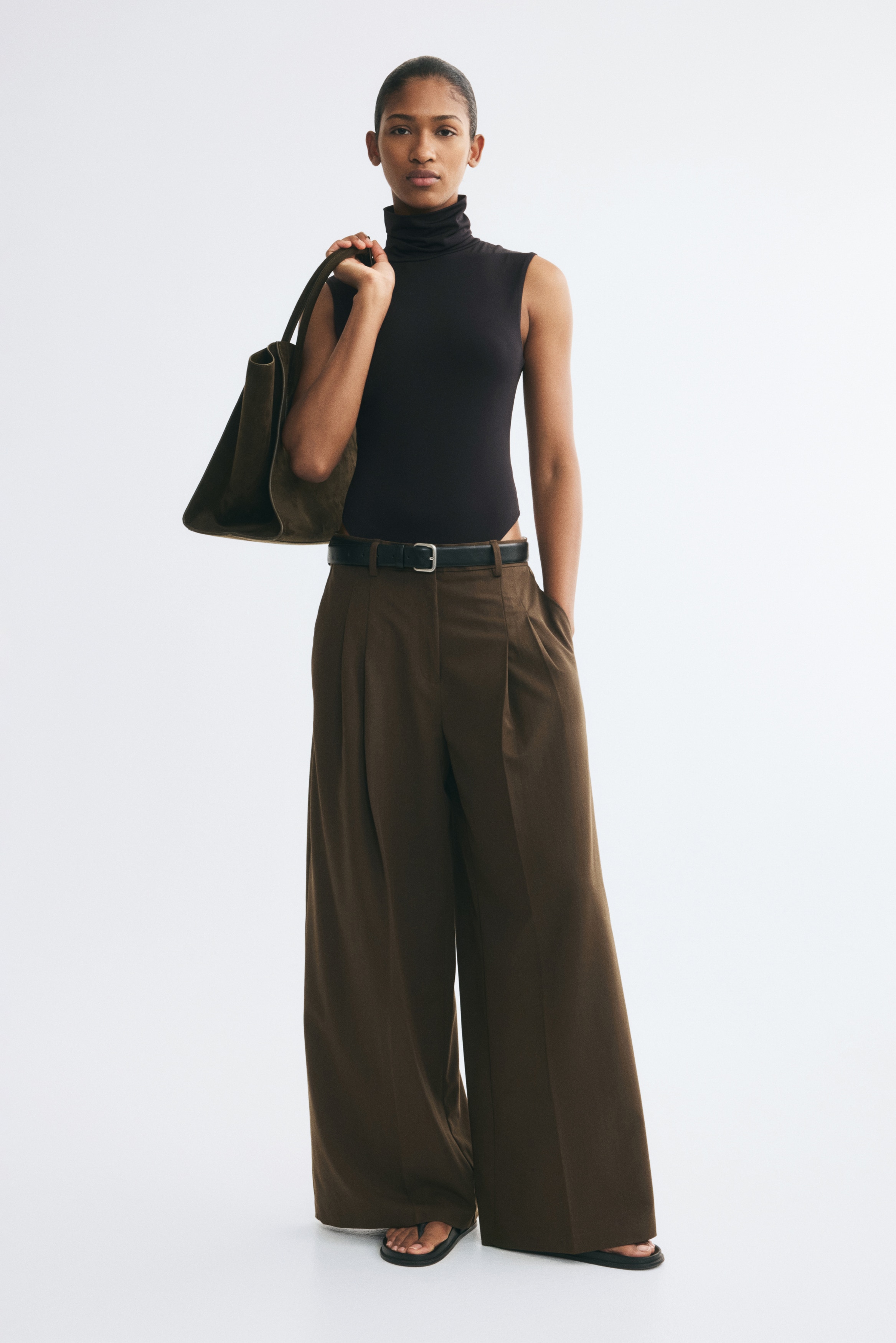 A black sleeveless bodysuit is facing front, showcasing a high turtleneck and structured, slightly padded shoulders. The garment features a fitted silhouette that tapers down to a high-cut thong bottom.