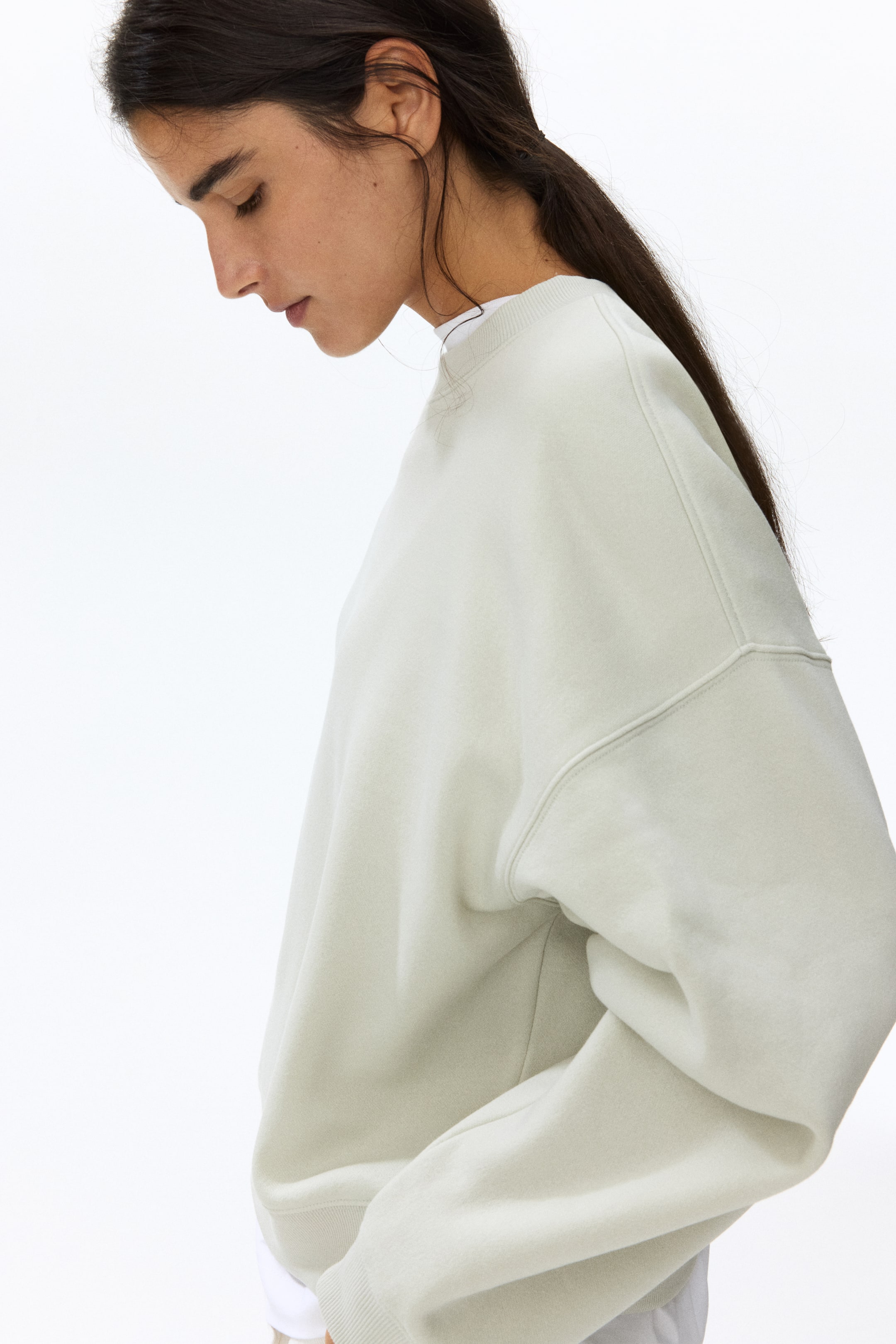 View larger image: A light green crew neck sweatshirt, shown from the side, features a relaxed fit with raglan sleeves and visible seam detailing. It showcases ribbed cuffs and a ribbed crew neckline, with a white t-shirt layered underneath and visible at the neckline.