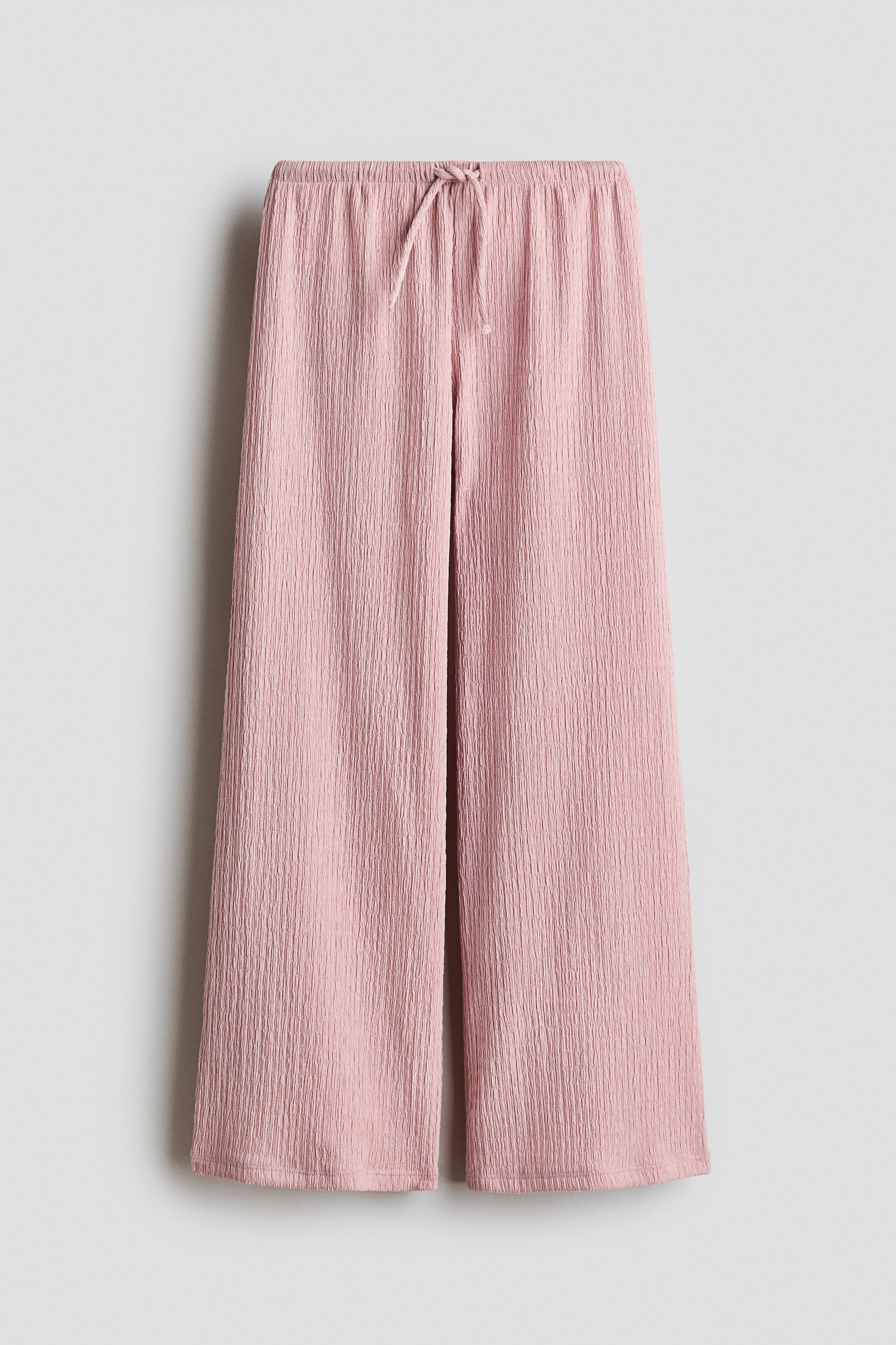 View larger image: Trousers in a soft pink, textured jersey are showcased from the FRONT. They feature an elasticated, drawstring waist with the drawstring tied, and straight legs.