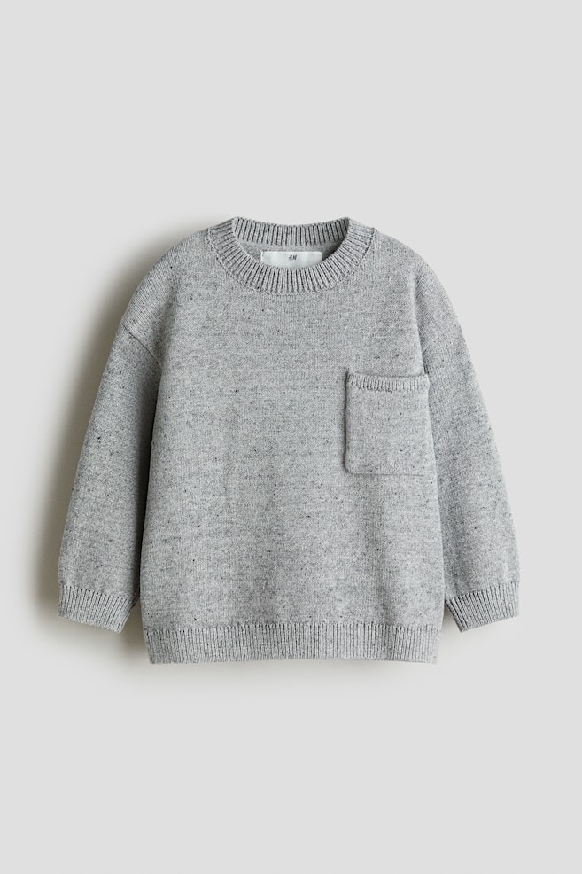 A grey fine-knit jumper is being presented as a FRONT view, featuring a subtle speckled pattern, a round rib-trimmed neckline, dropped shoulders, long sleeves, a rectangular patch chest pocket positioned on the left chest, and visible ribbing at the cuffs and hem. - 1