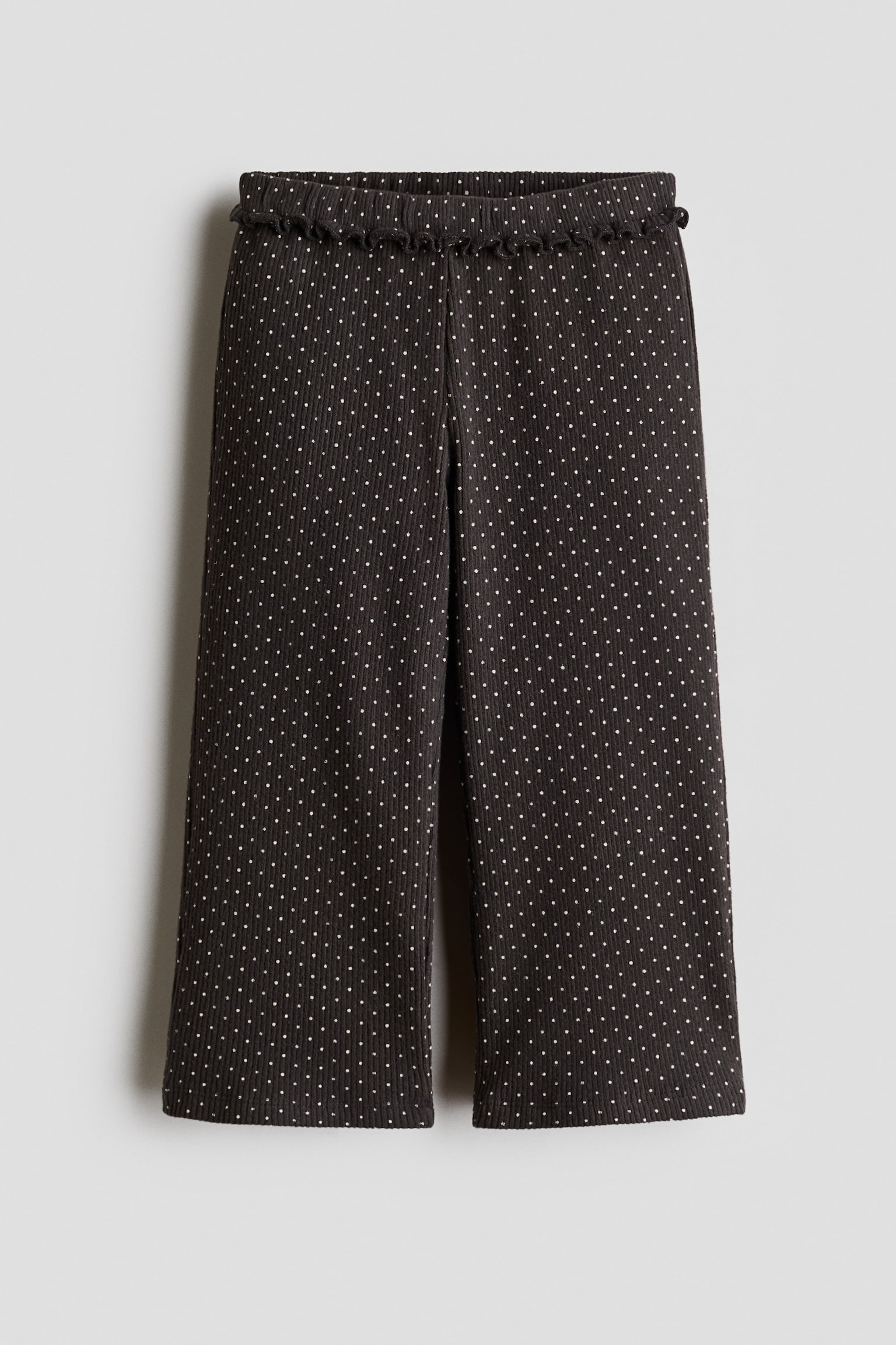 Ce pantalon large gris foncÃ©, ornÃ© dâun motif Ã  pois blancs sur lâensemble, est prÃ©sentÃ© de face, mettant en valeur une texture cÃ´telÃ©e ainsi quâune taille Ã©lastiquÃ©e Ã  bordure volantÃ©e.