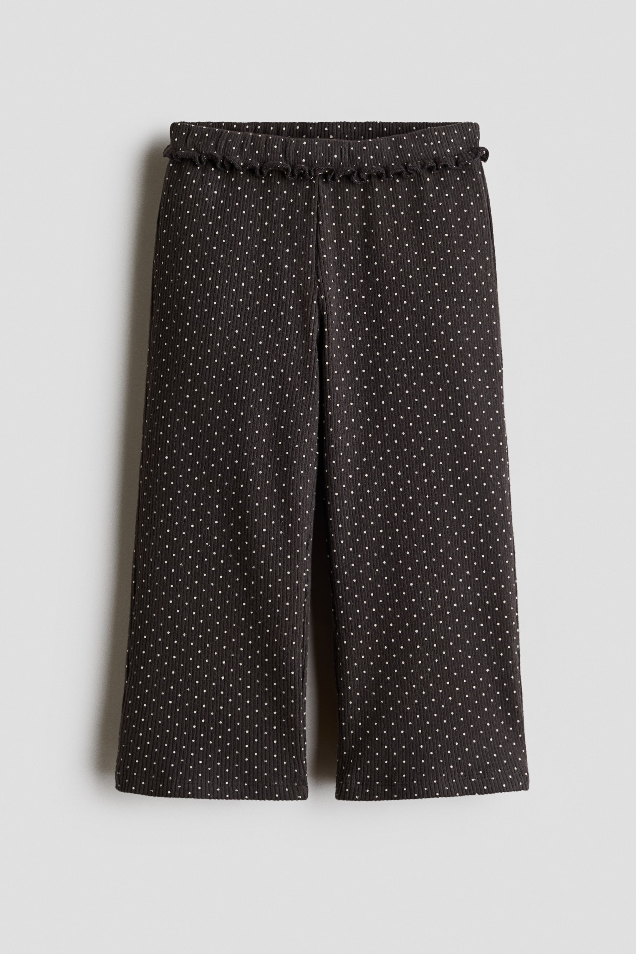 View larger image: These dark grey, wide-leg trousers featuring an all-over white polka-dot pattern are presented from the front, showcasing a ribbed texture and an elasticated, frill-trimmed waistband.