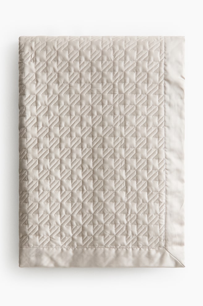 A light beige quilted blanket featuring a geometric stitch pattern across its main body, with a smooth, unquilted border framing the edges. - 1