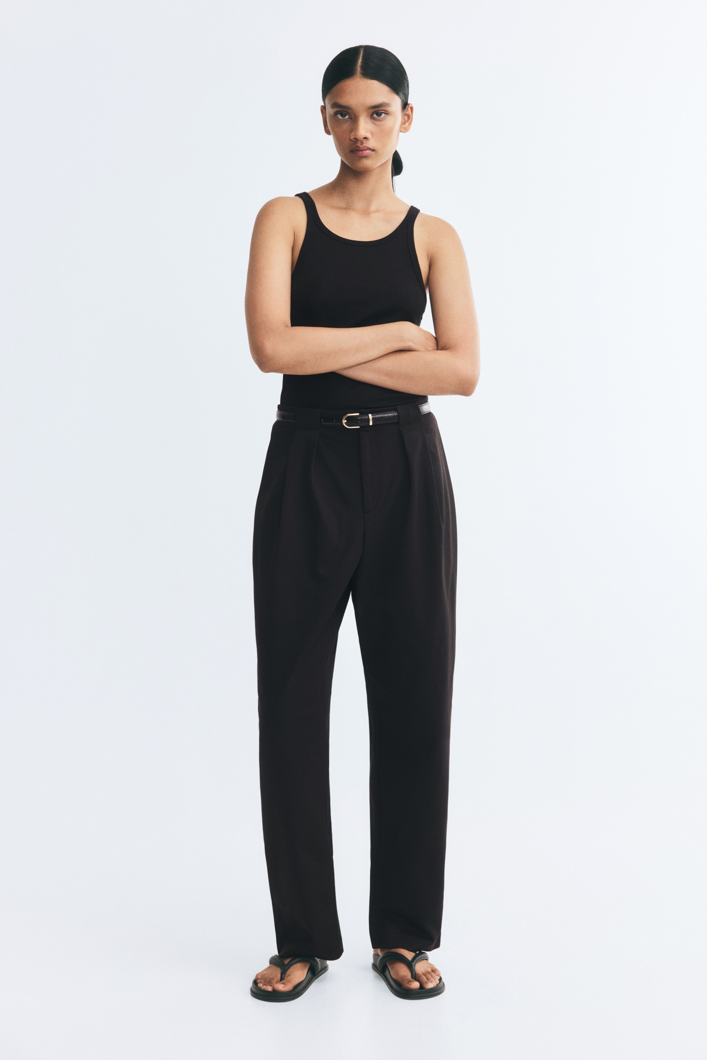 Crne krojene pantalone prikazane su spreda, sa Äistim pojasom, prednjim faltama i skrivenim Å¡licem. Pantalone su dizajnirane sa blago suÅ¾enim nogavicama koje imaju diskretan pregib duÅ¾ sredine.