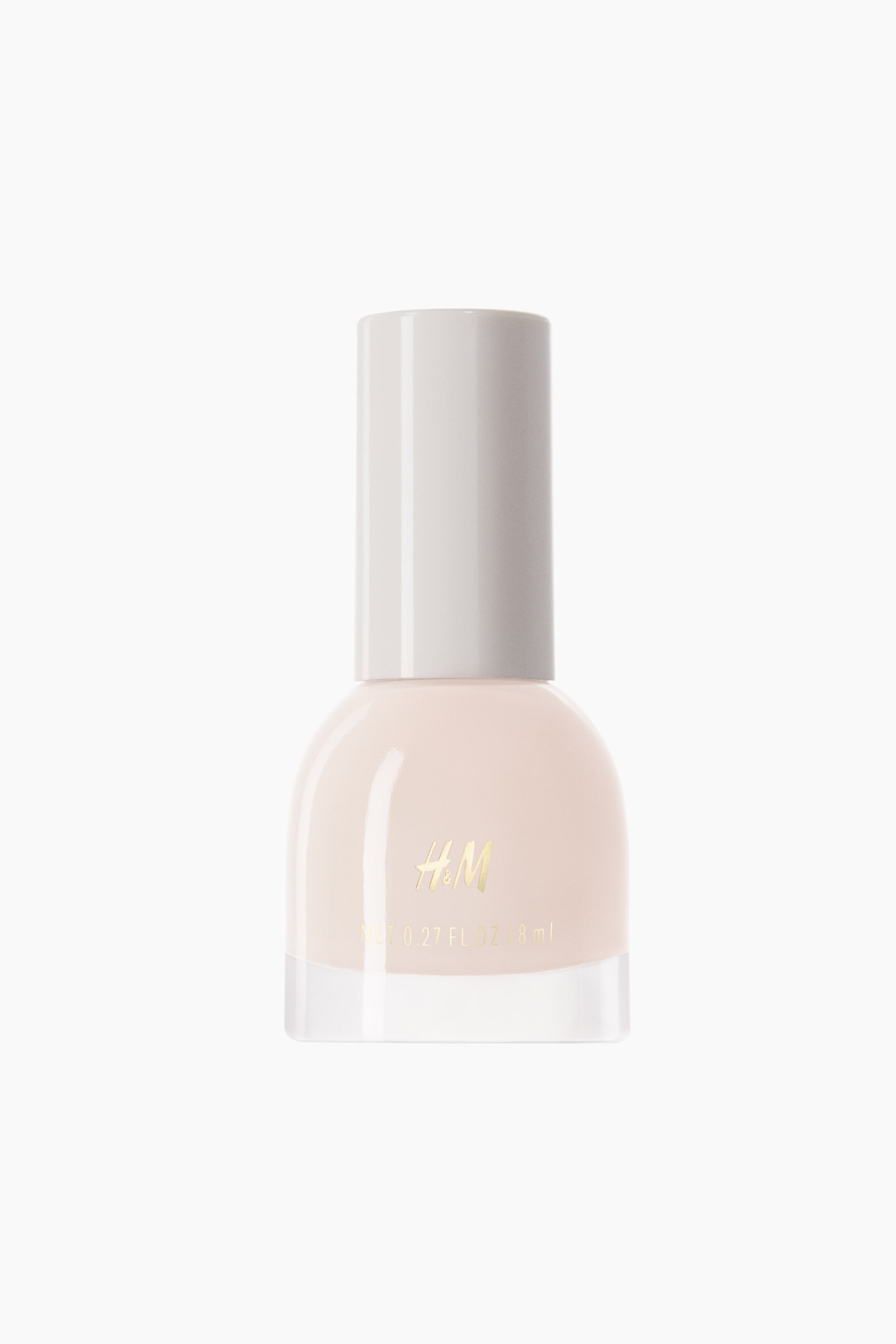 View larger image: A bottle of pale pink nail polish stands upright, shown from the front with its rounded glass body, thick clear base, and tall cylindrical off-white cap. The front of the bottle displays a gold-toned logo and product volume details.
