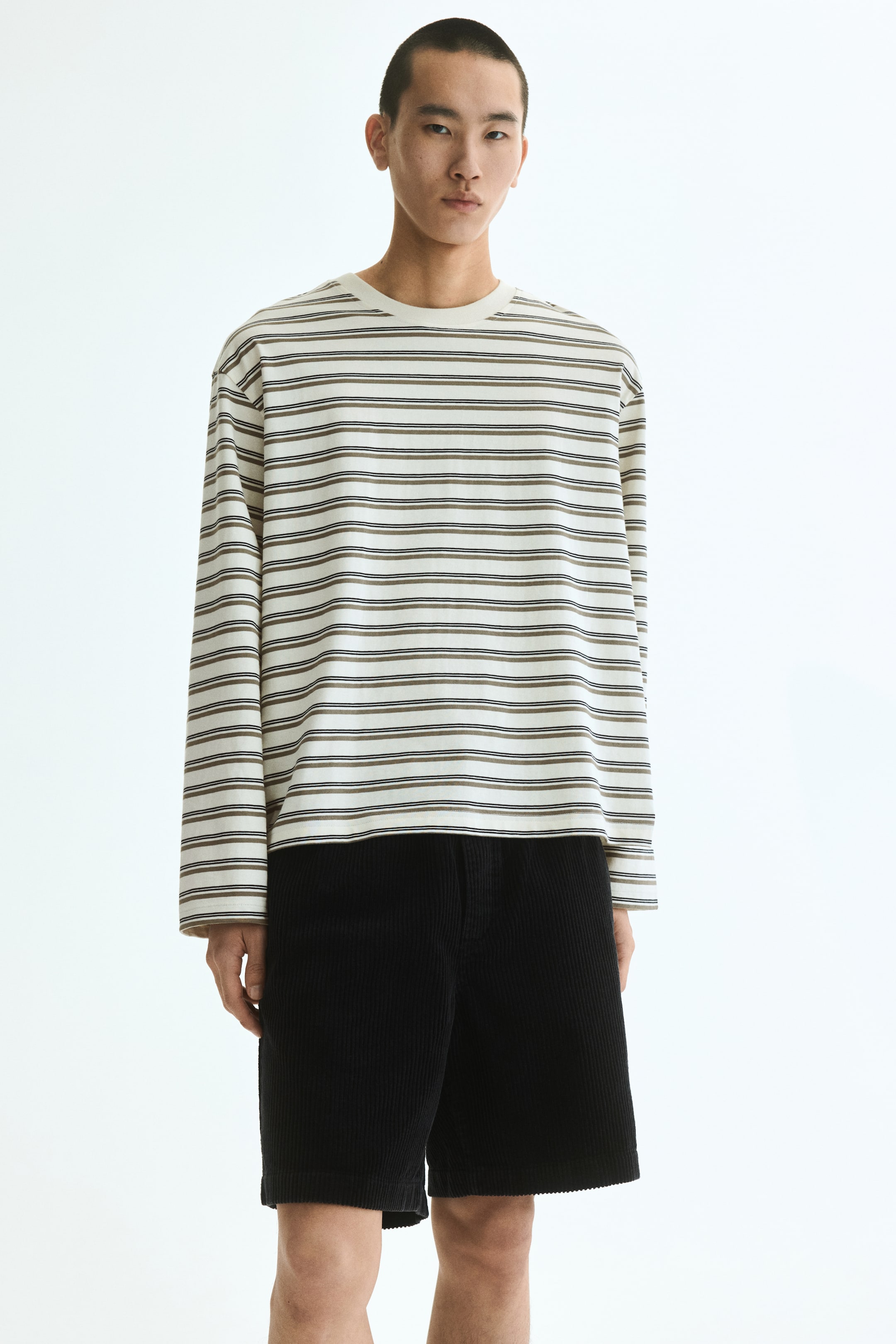 Grotere afbeelding bekijken: Een T-shirt met lange mouwen in een boxy-stijl van katoenen jersey wordt van voren gepresenteerd. Het is wit met donkere horizontale strepen, heeft een ronde hals met ribboord, verlaagde schouders en een recht gesneden zoom, wat een ontspannen pasvorm laat zien.