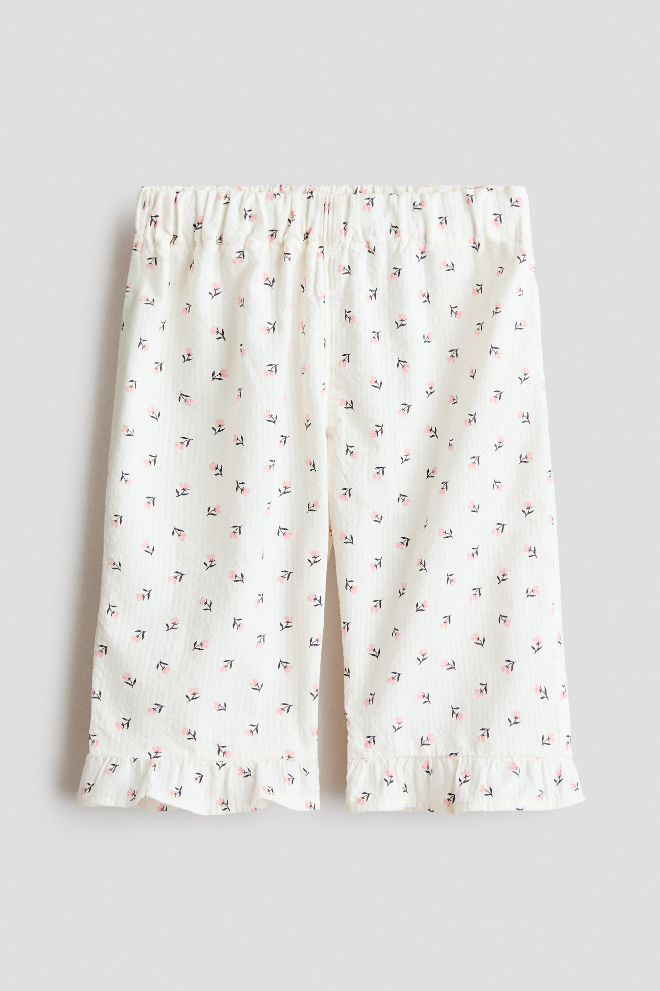 Agrandir l'image: Ce pantalon présente un tissu crème subtilement texturé avec un petit motif floral rose répétitif, face avant. Il est doté d'une taille élastiquée et de jambes larges, se terminant par des ourlets à volants.