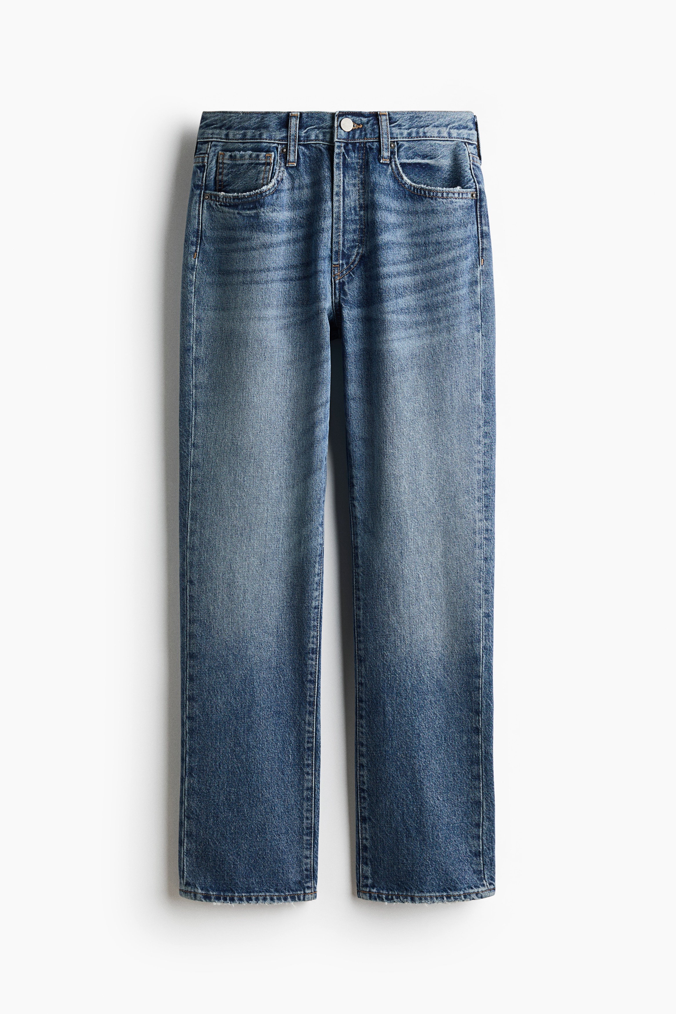 Jeans de ganga azul de corte direito, em lavagem mÃ©dia, sÃ£o usados pelo modelo, que descansa uma mÃ£o no bolso frontal. As jeans apresentam cintura normal e estÃ£o combinadas com um blazer preto estruturado e de corte alfaiatado.