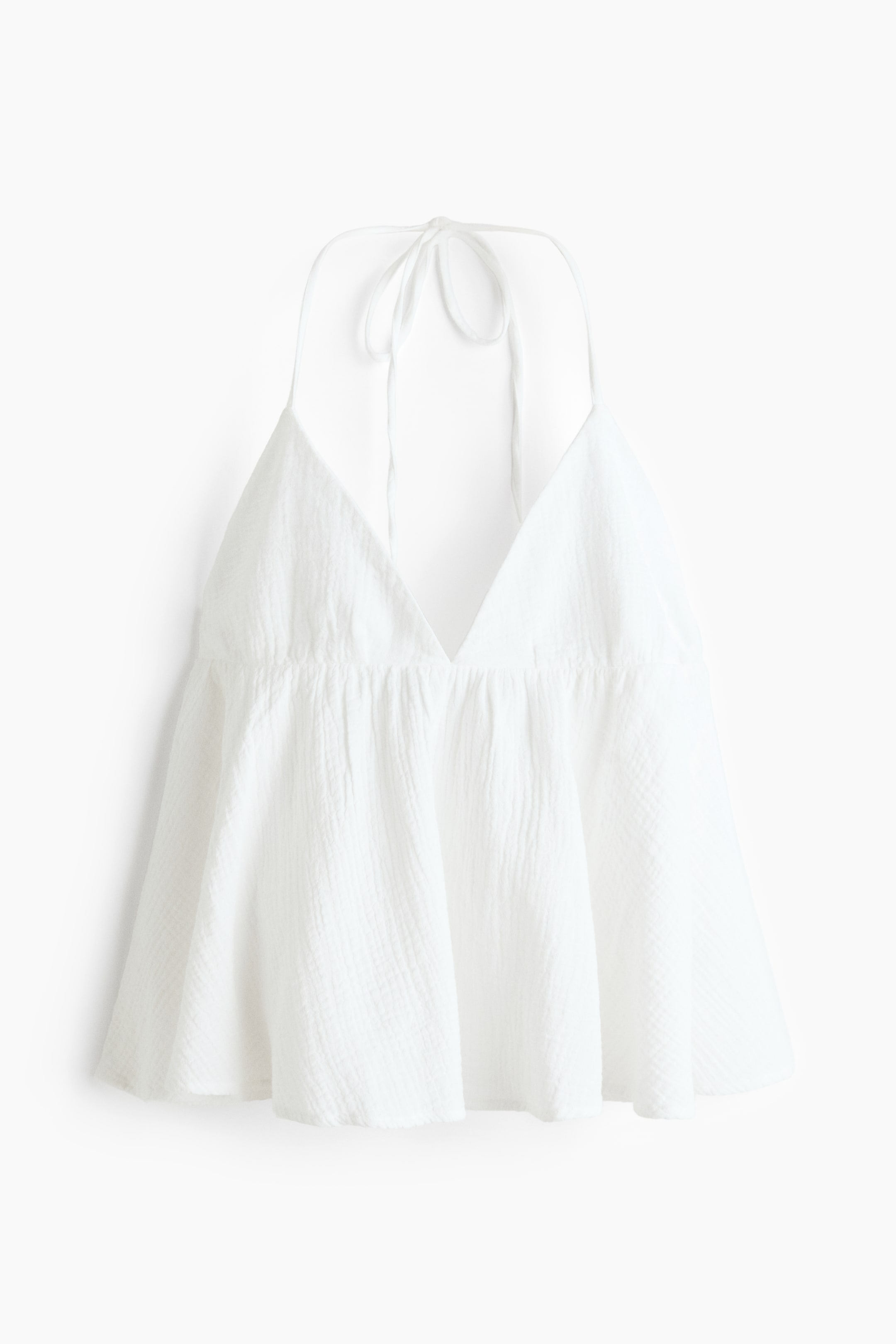 View larger image: A white cotton muslin top is showcased from the front, highlighting a V-neckline with halterneck ties. A gathered seam is visible below the bust, forming a flared silhouette.