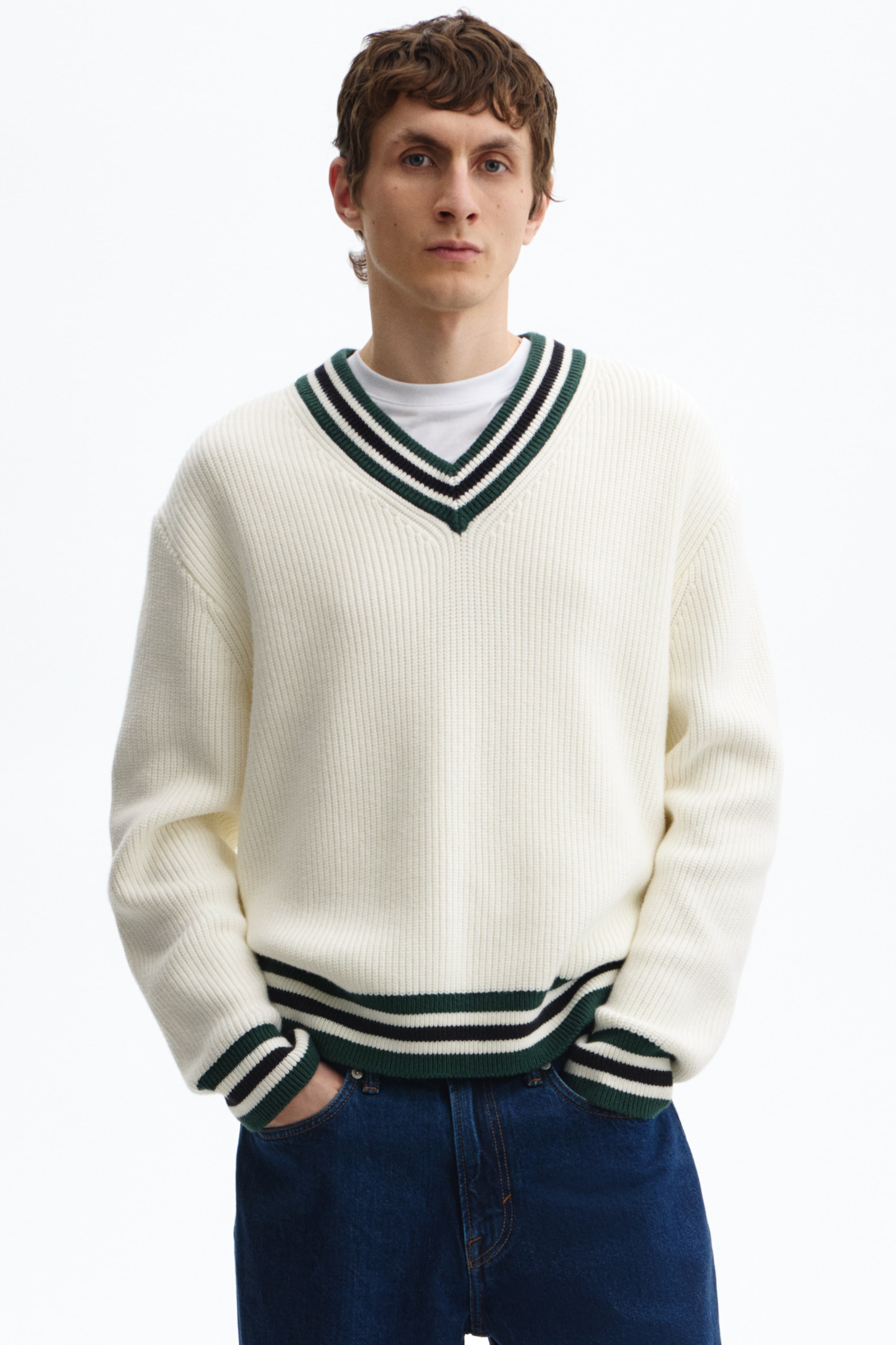 View larger image: A cream ribbed knit V-neck sweater featuring green and black stripes along the V-neck, with ribbed cuffs and a ribbed hem, is worn over a white T-shirt.