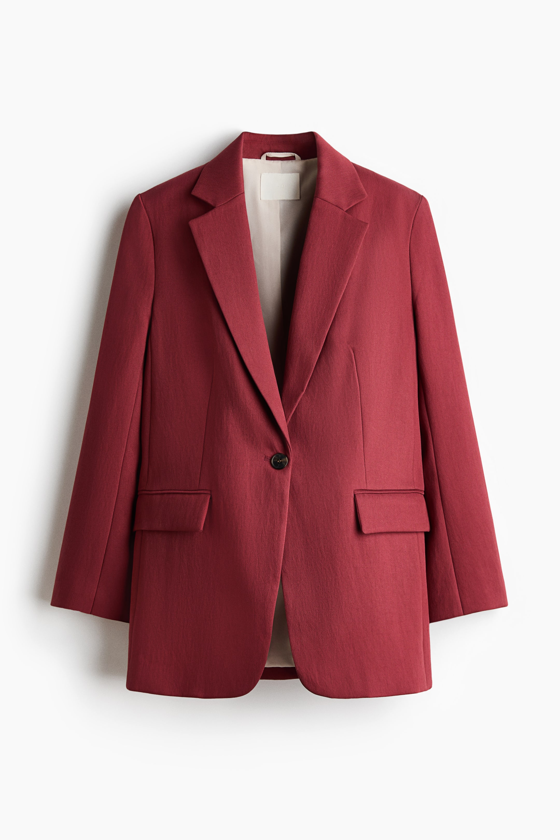 View larger image: A deep red blazer is facing front, featuring notch lapels and a single-button closure with a dark button. Two flap pockets are visible on the front, and a light-colored lining is showing around the collar and inside the open front.