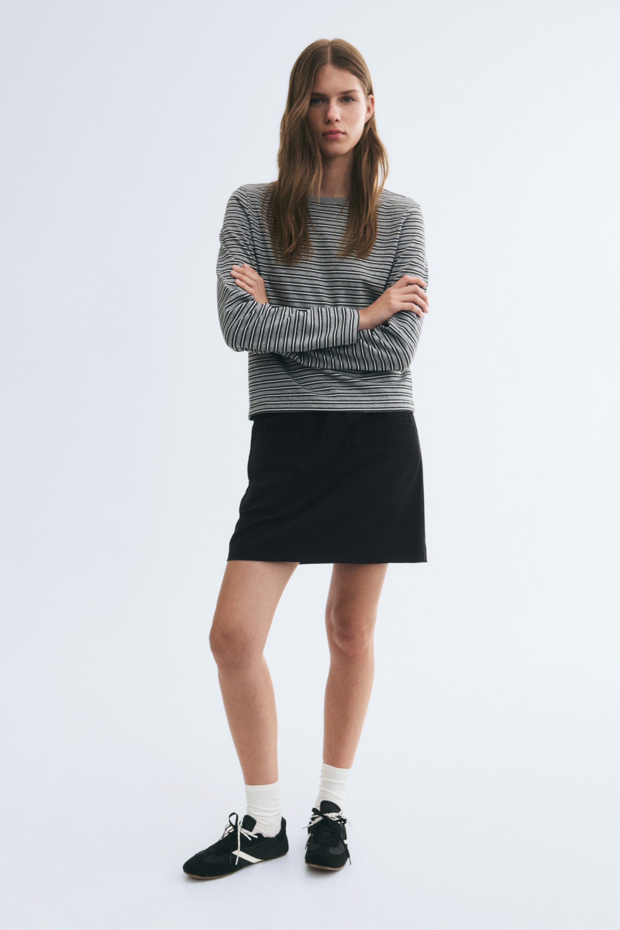 View larger image: The model is wearing a short black fitted skirt styled with a long-sleeved grey and black striped top that overlaps the waistband. The skirt features a straight silhouette and a clean, minimalist design.