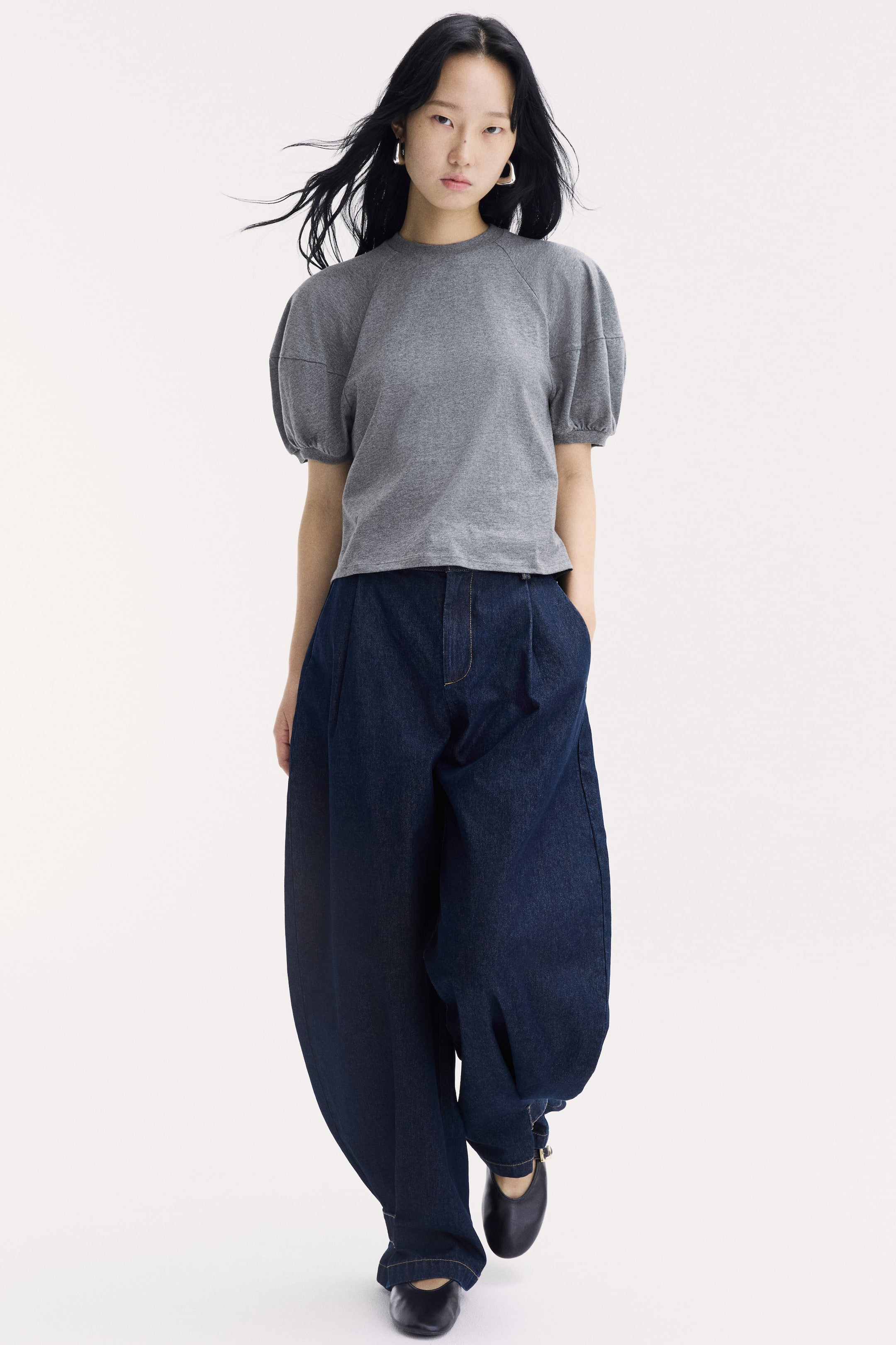 View larger image: A grey cotton jersey top featuring a round, rib-trimmed neckline and short puff sleeves in a raglan cut with ribbed cuffs is being worn by the model. The top is paired with wide-leg, dark blue denim trousers.