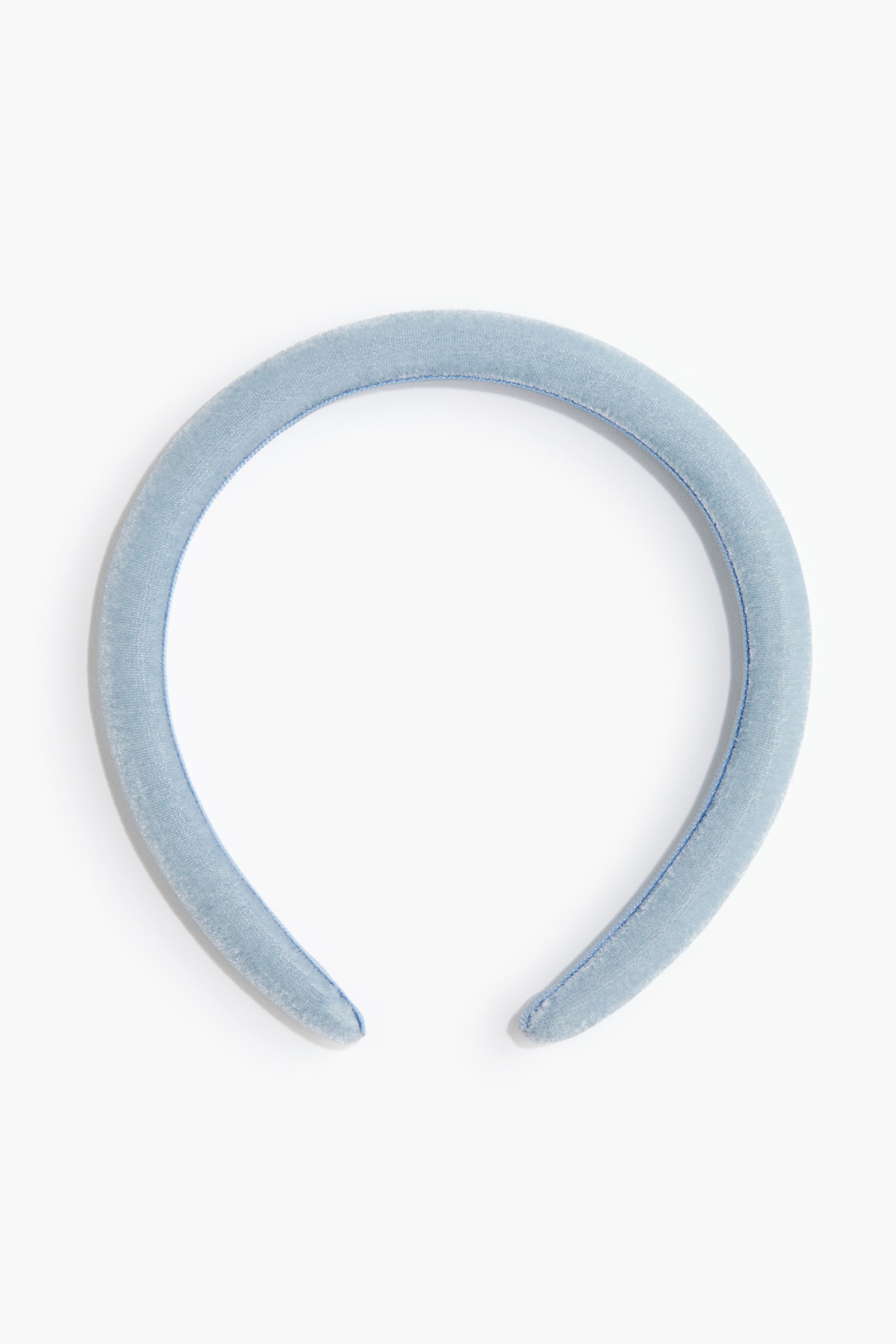 Grotere afbeelding bekijken: Een gewatteerde lichtblauwe fluwelen haarband buigt in een U-vorm, met zichtbaar blauw stiksel langs de buitenranden.