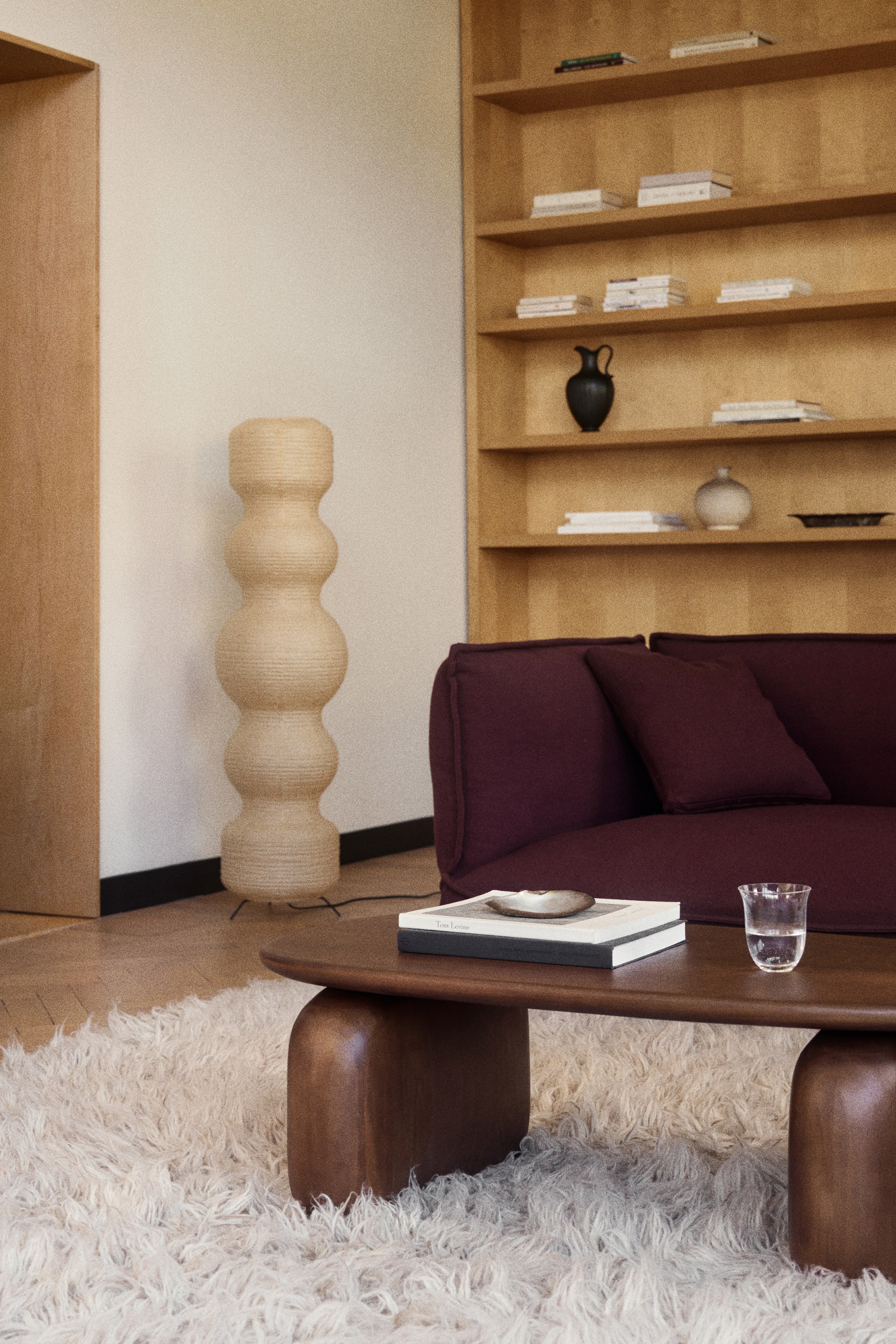 View larger image: An angled view of a dark wood coffee table showcases a rectangular tabletop with rounded edges and wide, sturdy legs with smooth, rounded contours. The table supports a book with a small dish on top and a glass of water on its surface, highlighting its organic design and smooth finish.