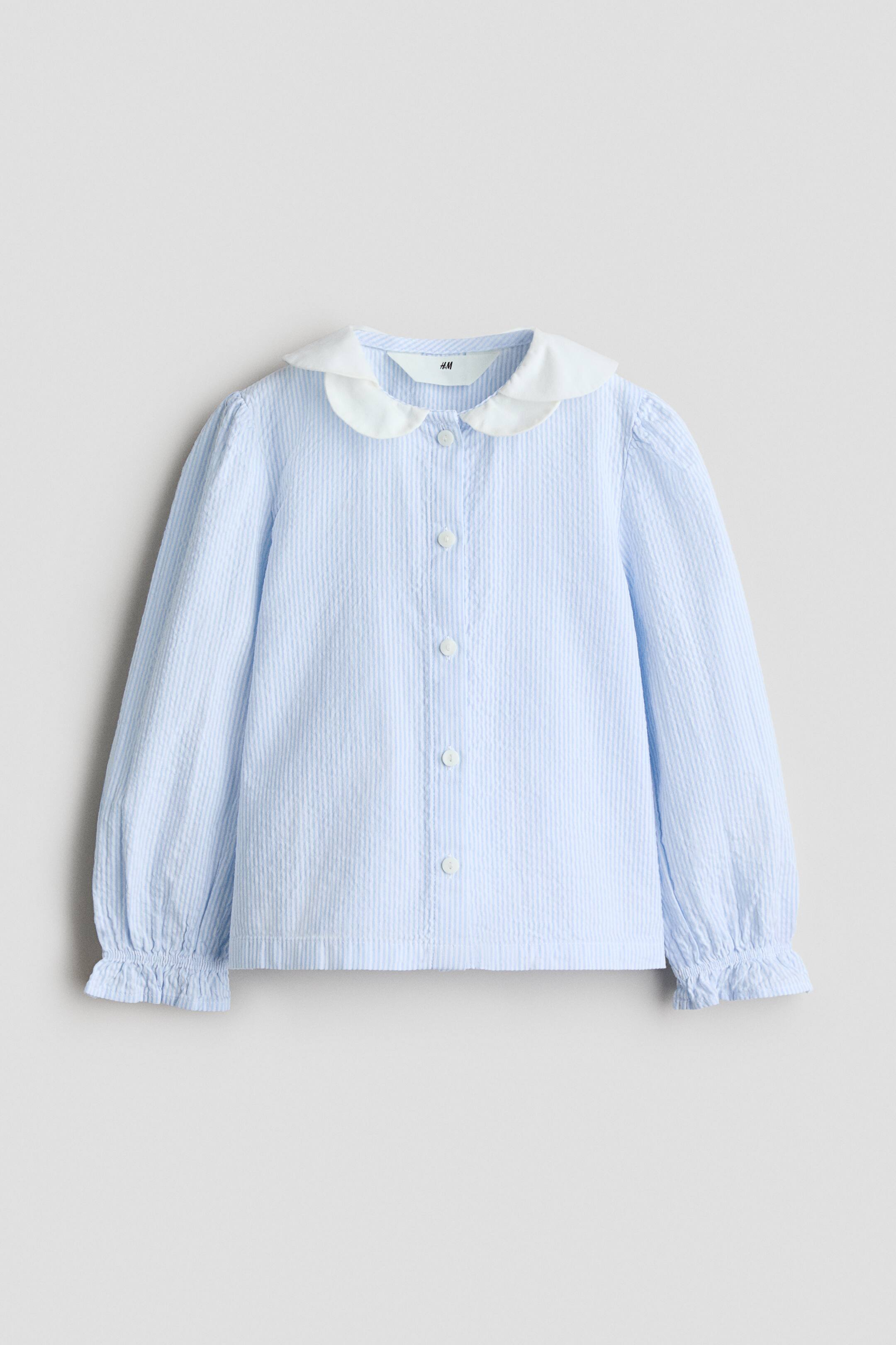 View larger image: A light blue textured long-sleeved shirt features a white rounded Peter Pan collar and a front button placket with white buttons. The sleeves feature subtle puff detailing at the shoulders and gathered, ruffled cuffs.