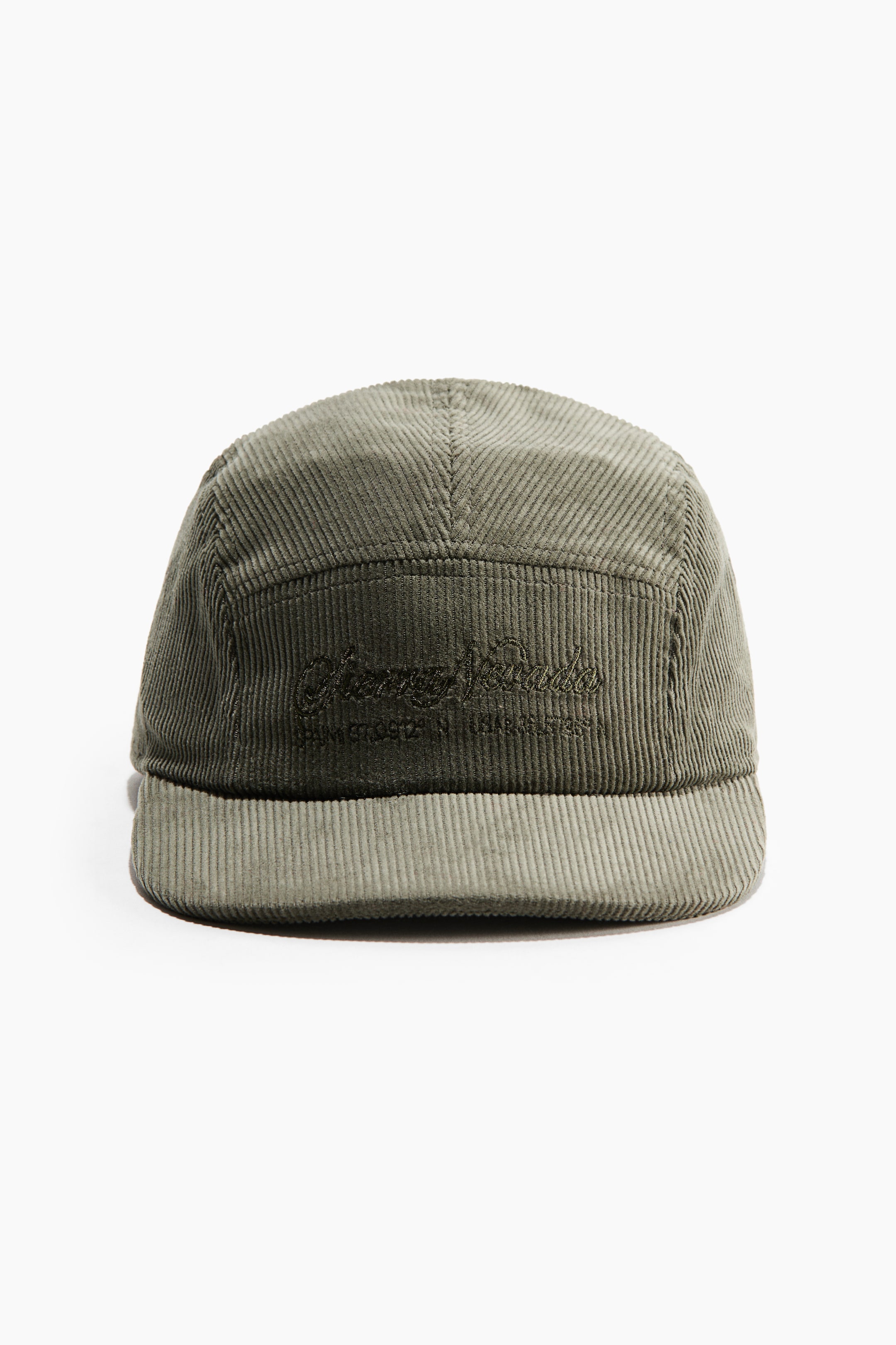 View larger image: A five-panel cap made of olive-green corduroy is shown front-facing, displaying its distinctive ribbed texture and flat brim. The front panel features a tone-on-tone embroidered script logo with geographic coordinates stitched underneath.