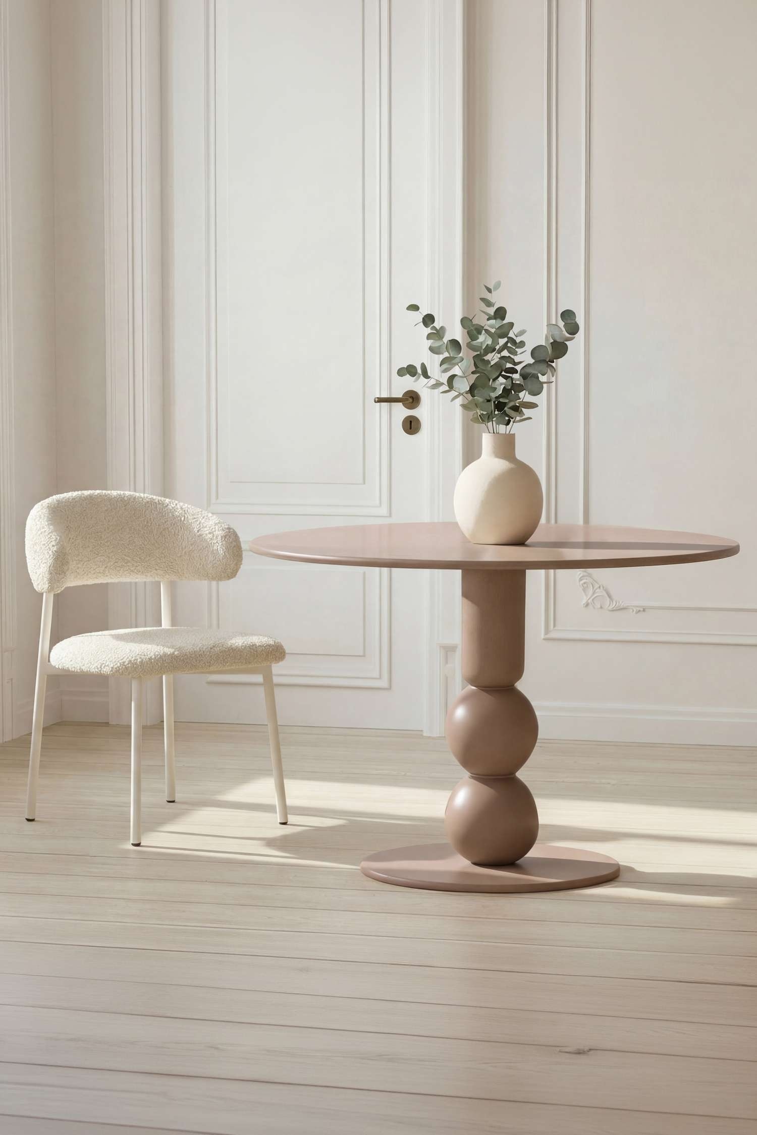 Il tavolo rotondo in beige tenue presenta un piano rotondo e una base centrale a piedistallo caratterizzata da una sezione cilindrica, due forme sferiche sovrapposte e una base rotonda piatta più ampia. Il tavolo è rivolto in avanti.