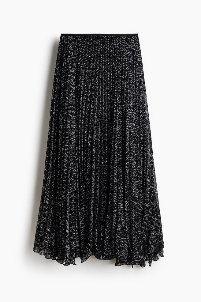 A black, ankle-length pleated skirt with a white polka-dot pattern is hanging in a front view, displaying a high, narrow elastic waistband. The sheer, pleated fabric is draping into a loose-fit silhouette that finishes with a wavy, asymmetrical overlocked hem. - 1