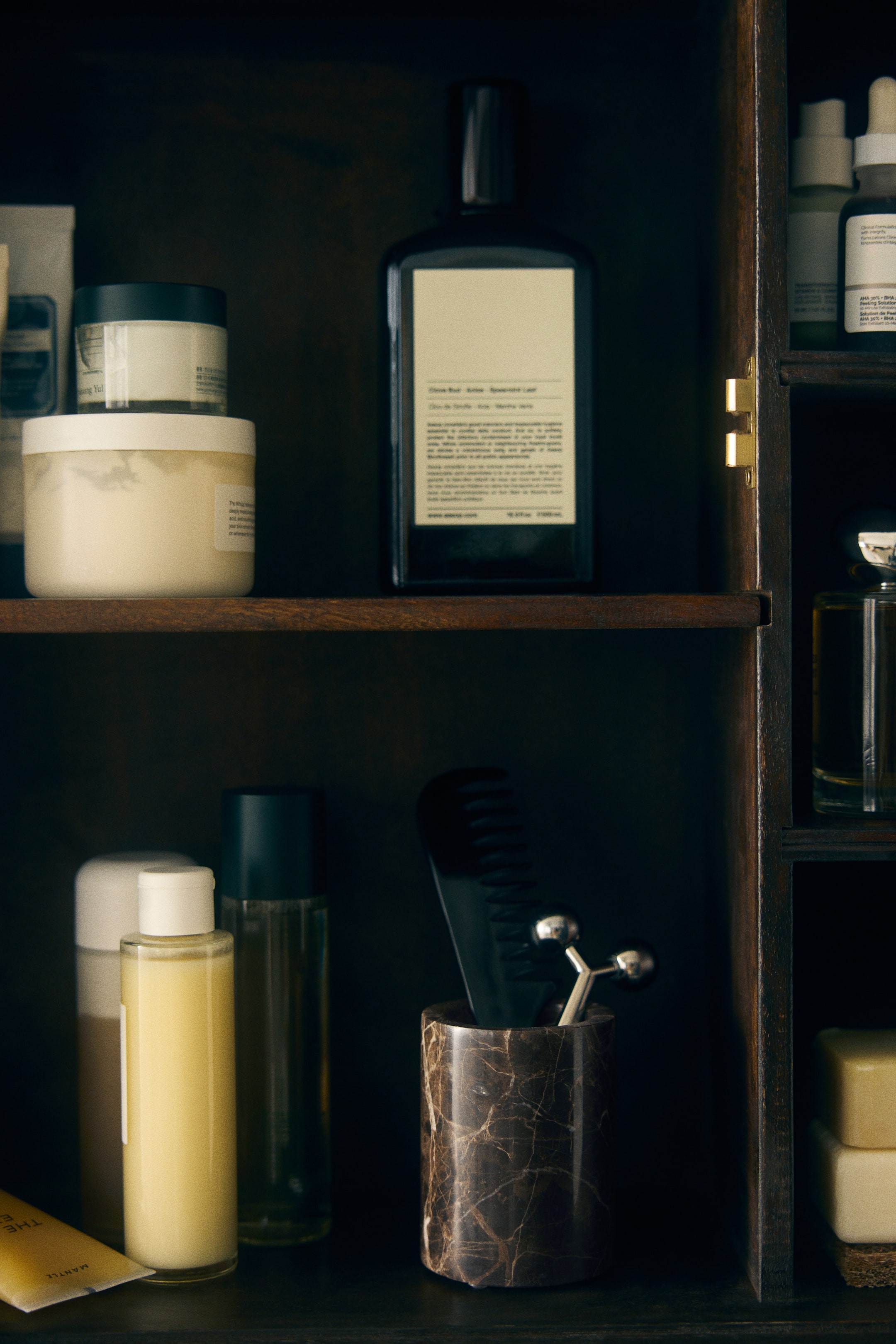View larger image: A cylindrical dark brown marble holder featuring natural tan and white veining is sitting on a shelf, holding a black comb and a silver-toned facial roller.