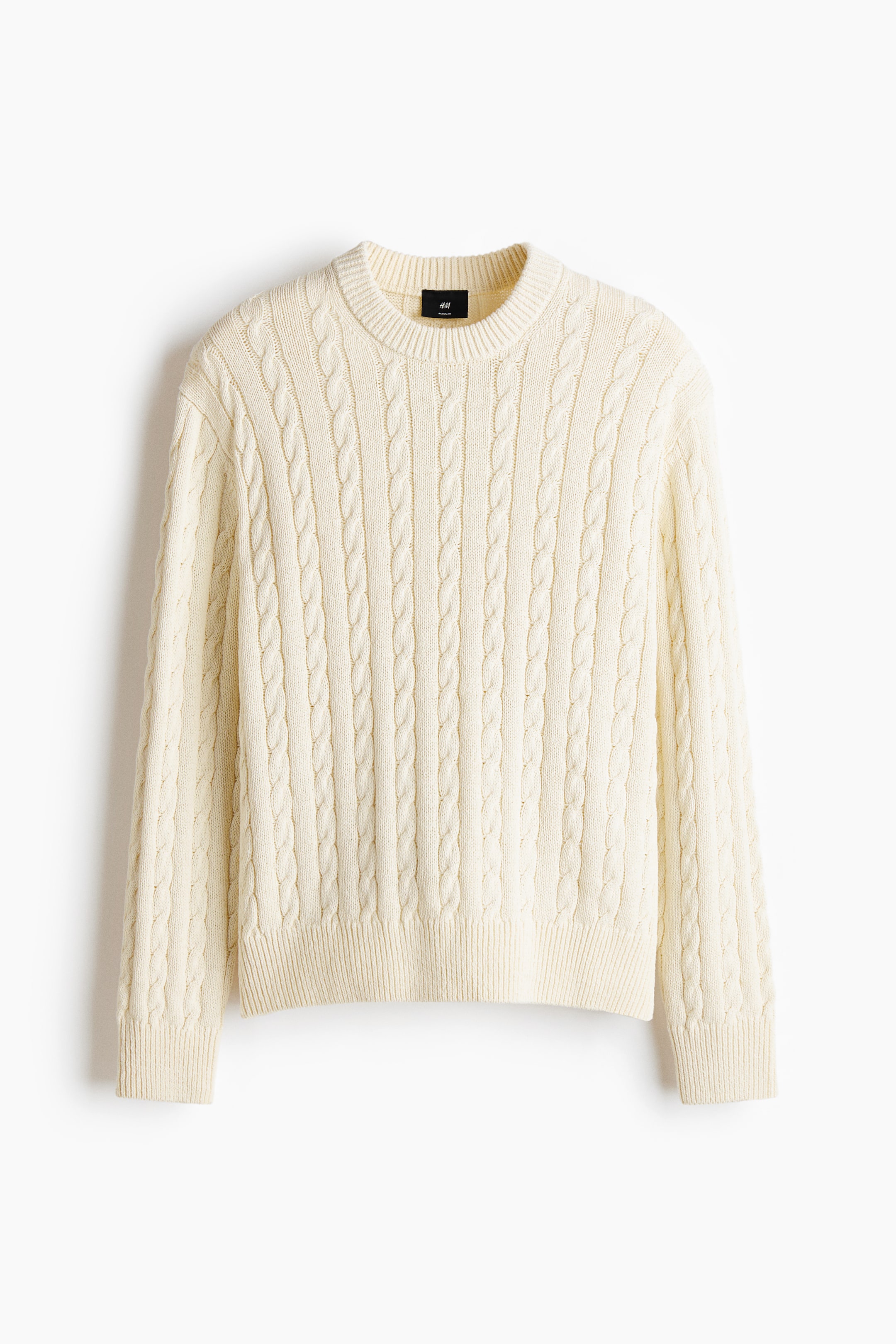 View larger image: A cream cable-knit sweater is displaying a crew neck, long sleeves with ribbed cuffs, and a ribbed hem, with a black brand tag visible at the back of the neck.