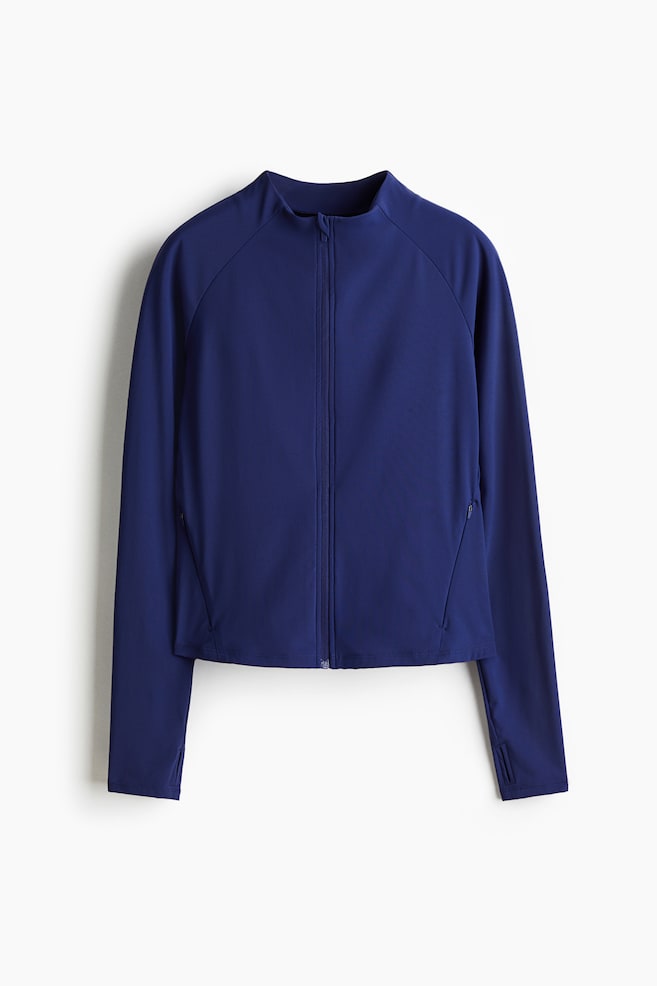 En mørkeblå nylon sportsjakke med DryMove? præsenteres forfra. En opretstående krave indrammer halsen, og en gennemgående tonal lynlås løber ned langs midten. Lange raglanærmer med tommelfingerhuller strækker sig, og en diskret lynlåslomme vises på den nederste højre side. - 1
