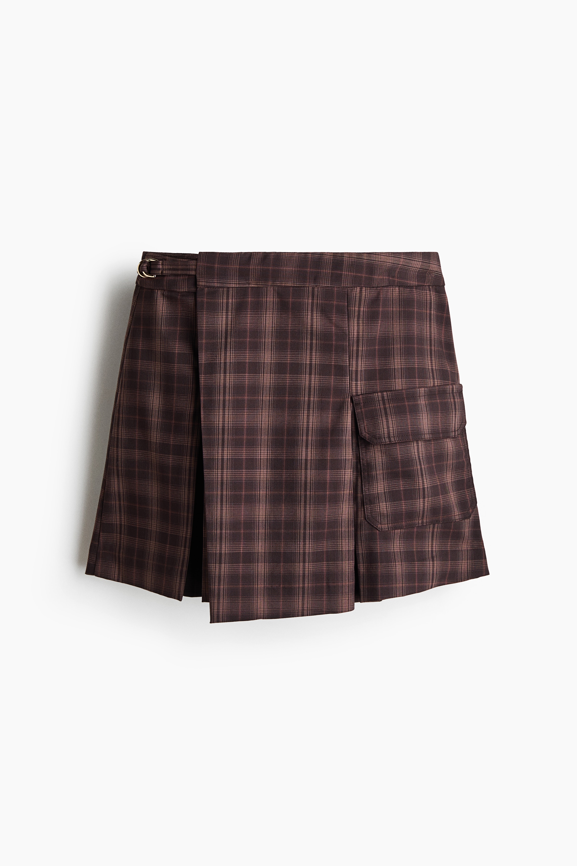 La modelo lleva una falda envolvente corta a cuadros cafÃ©, con frente cruzado, un solo bolsillo lateral con solapa y detalles plisados. La falda se combina con una blusa de manga larga color crema en capas y botas negras altas.