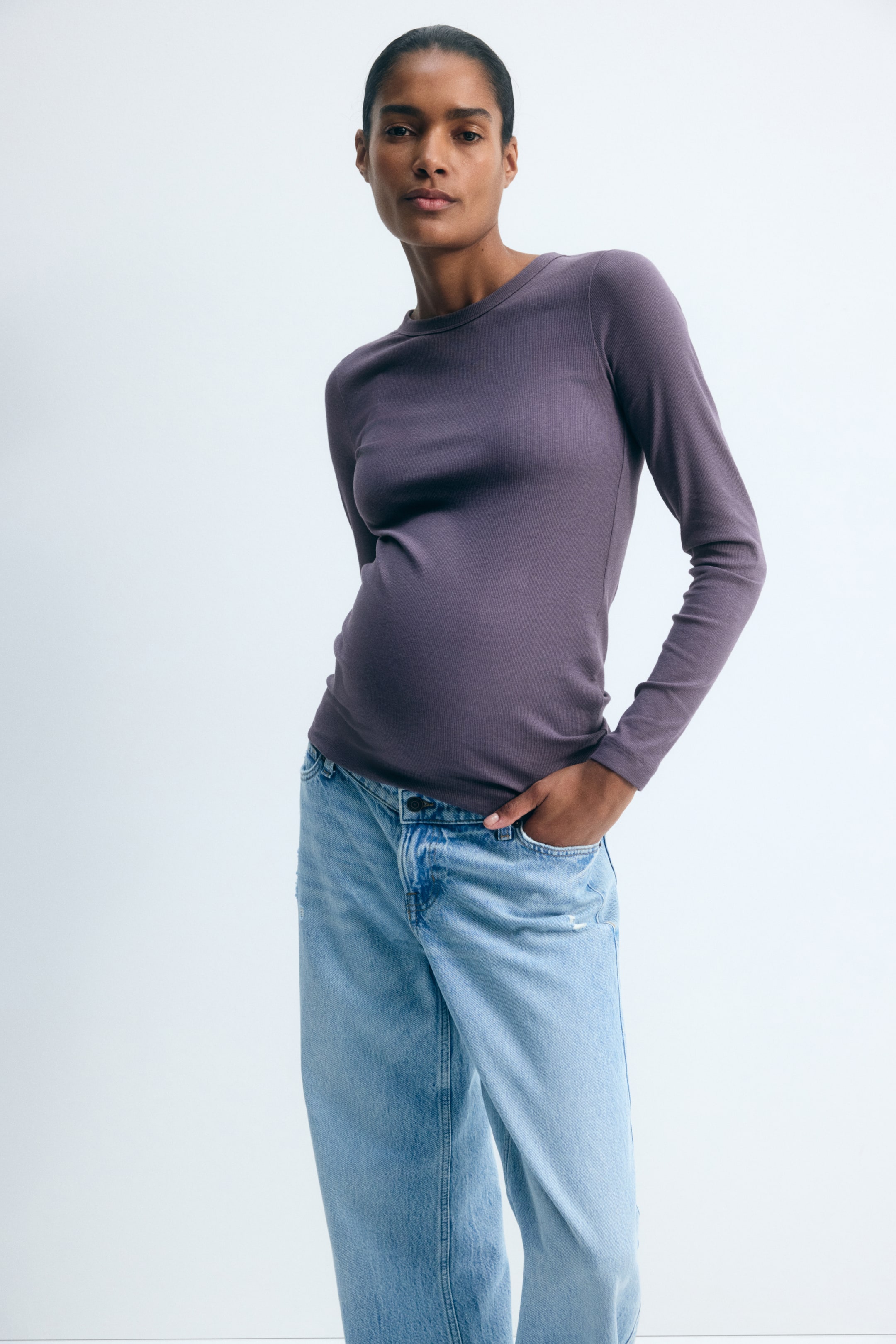 Voir une image plus grande: Le mannequin porte un haut violet ajusté à manches longues avec un col rond, et pose avec une main dans la poche d’un jean bleu délavé.