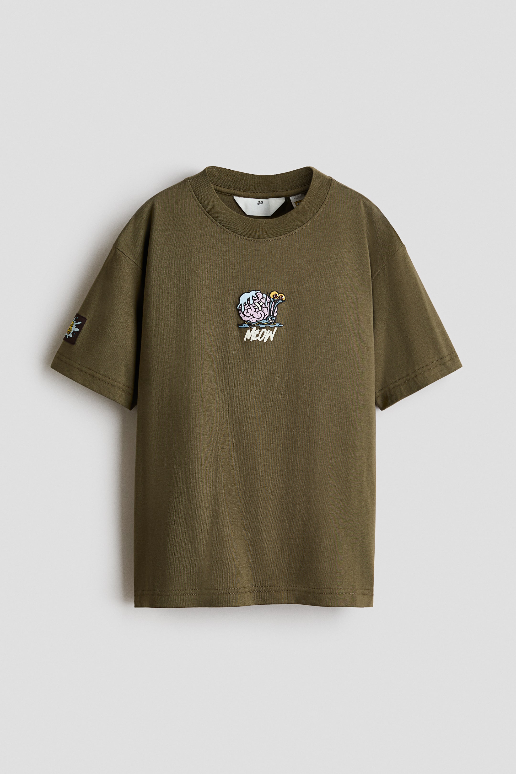 View larger image: An olive green cotton T-shirt is shown from the front, featuring a rib-trimmed crew neckline and dropped shoulders. The T-shirt displays a small cartoon graphic at the center chest with the word "MEOW" printed below it, along with a small black patch on the right sleeve.