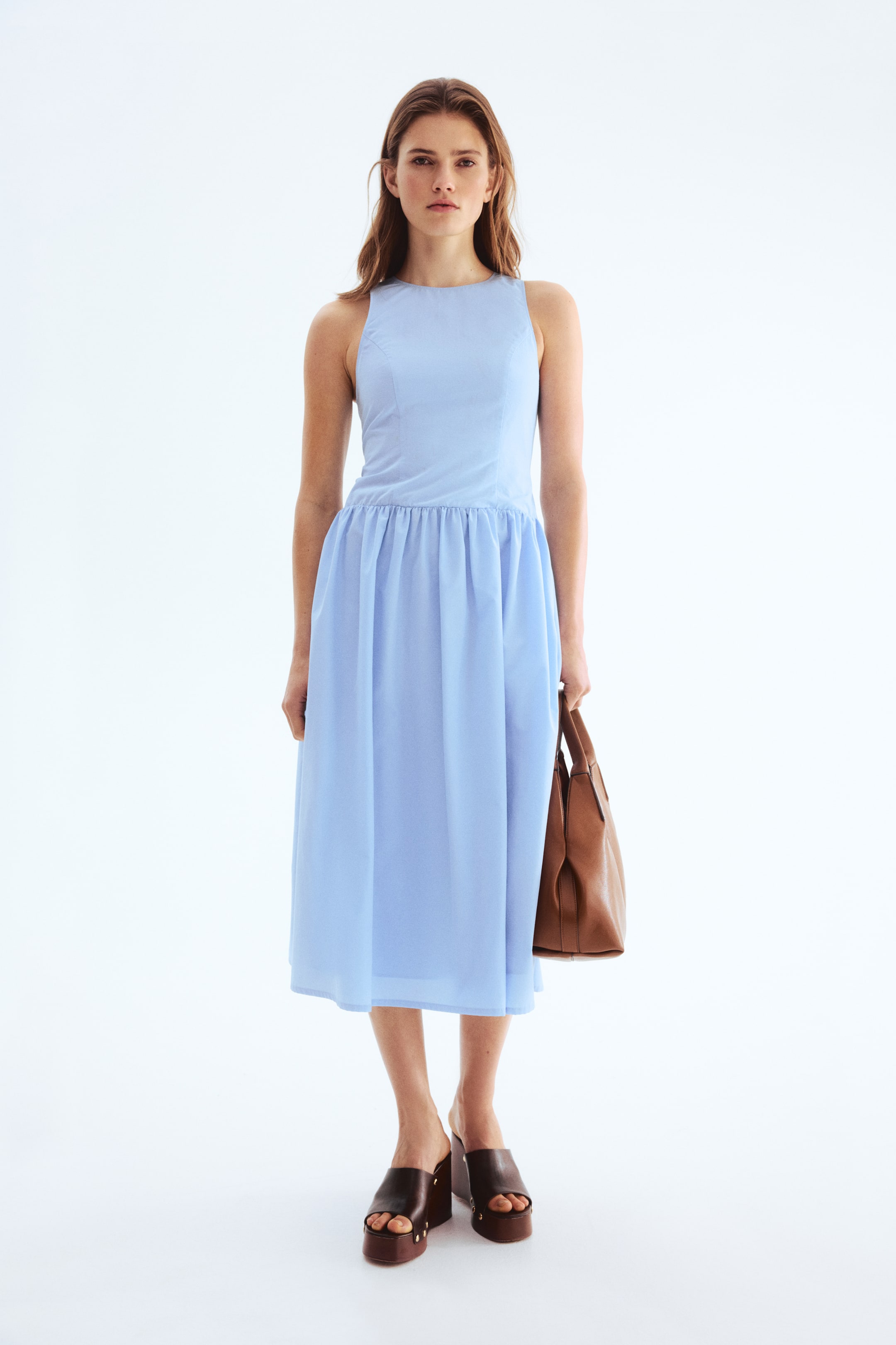 Xem ảnh lớn hơn: Chiếc váy không tay màu xanh nhạt có đặc điểm là cổ tròn, thân váy ôm sát, eo được xếp ly và chân váy chữ A dài đến giữa bắp chân.
