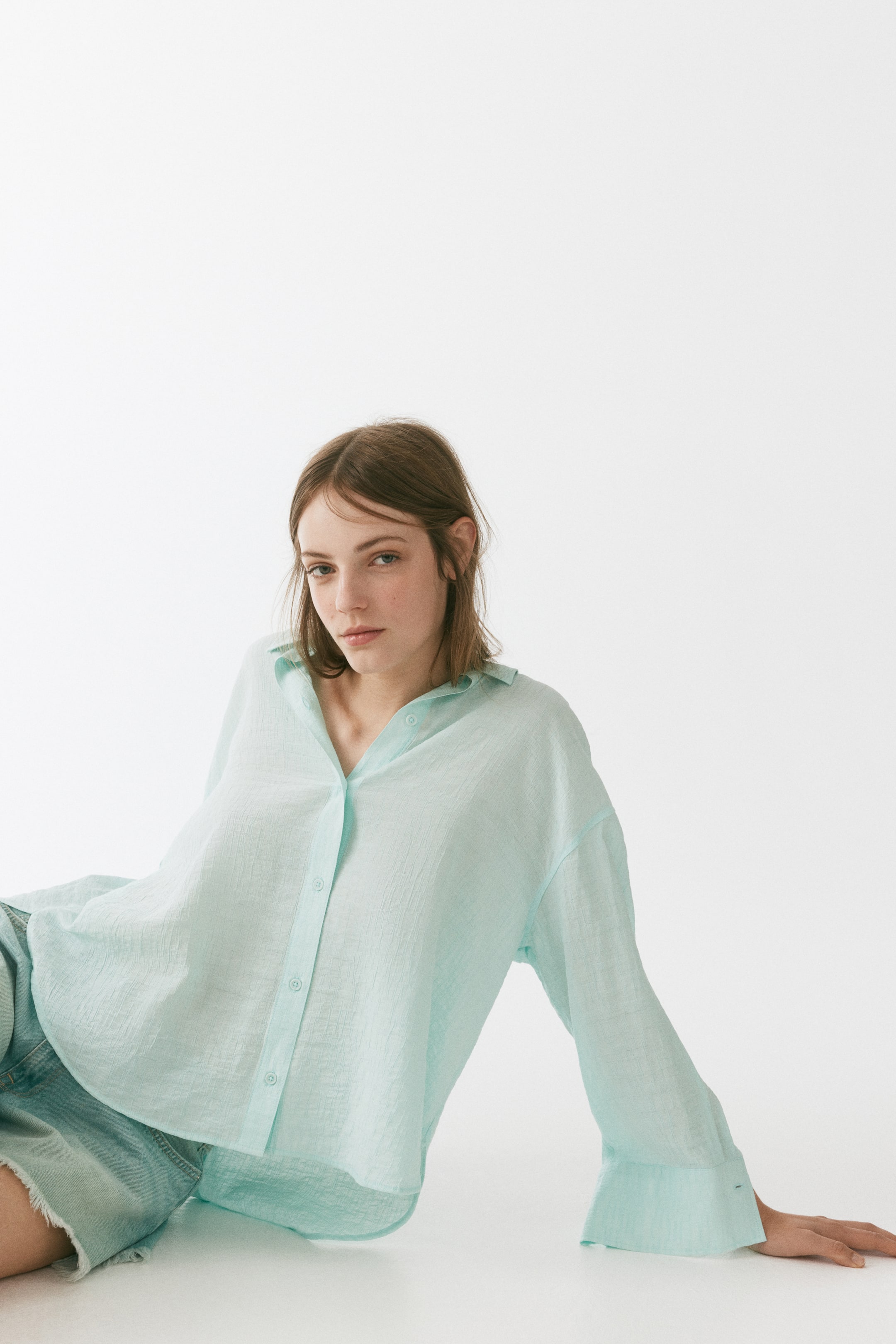 View larger image: A light blue, long-sleeved button-front shirt crafted from crinkled textured fabric, offering a relaxed, oversized fit. The pointed collar is left unbuttoned to create a V-neck, with front buttons partially undone.