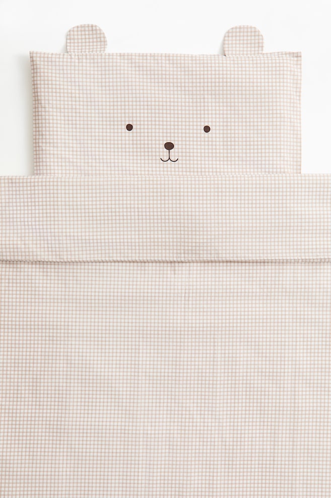 Ten dzieciÄcy komplet poÅcieli, sfotografowany z przodu, prezentuje beÅ¼owo-biaÅÄ kratÄ gingham, obejmujÄcÄ poszewkÄ na poduszkÄ z nadrukowanÄ minimalistycznÄ buziÄ misia oraz naszytymi materiaÅowymi uszami u gÃ³ry, a takÅ¼e dopasowany, zÅoÅ¼ony pokrowiec na koÅdrÄ. - 1