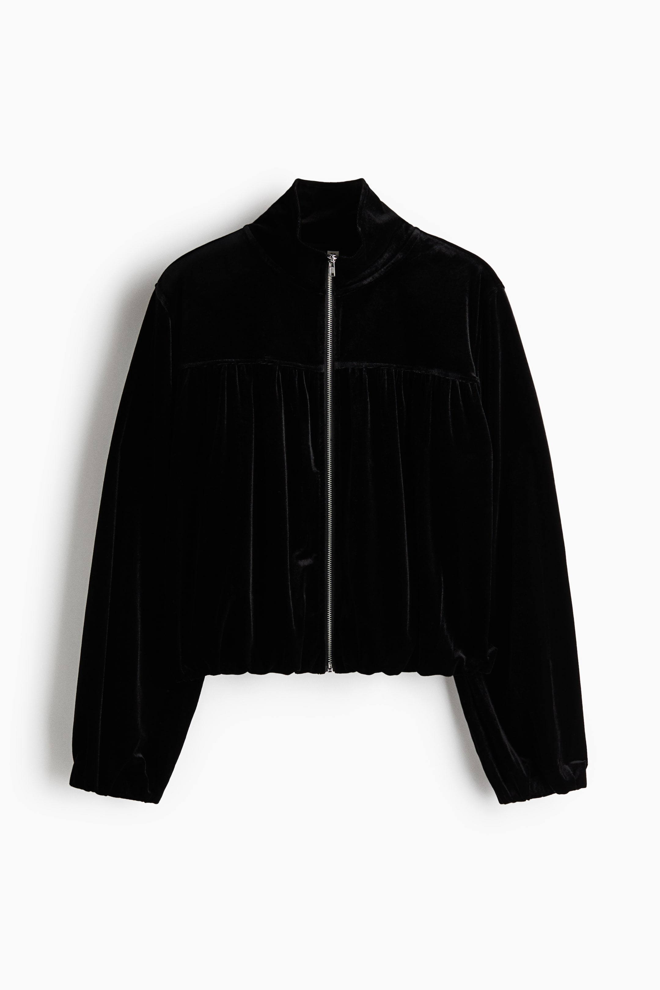 Ampliar la imagen: Se muestra una chaqueta de terciopelo negro de frente, con cuello alto simulado y un cierre de cremallera plateada de largo completo al centro. El diseño presenta un canesú horizontal en el pecho con tela fruncida que cae hasta un dobladillo elástico, acompañado de mangas largas con puños elásticos.