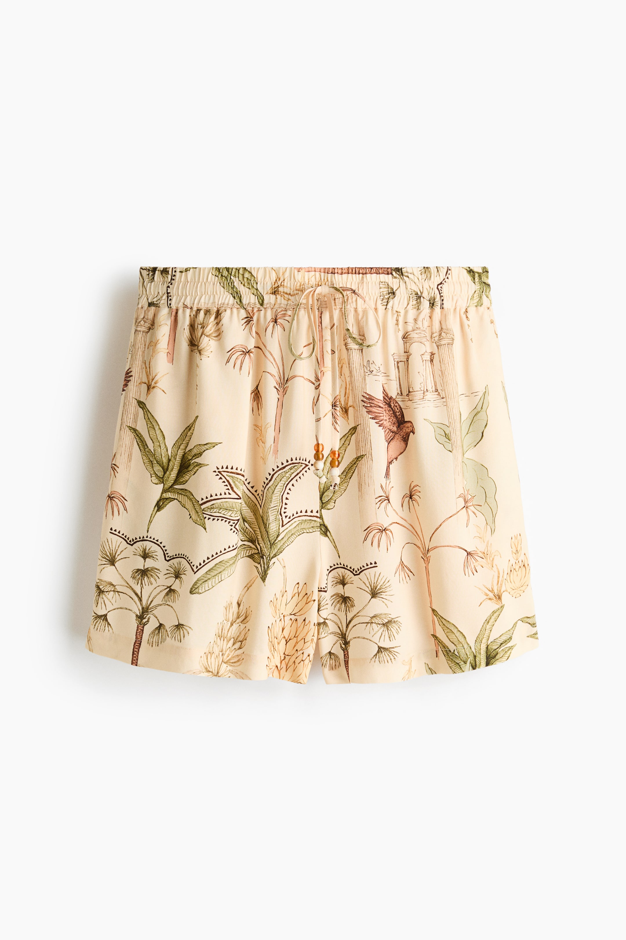 View larger image: Front-facing shorts feature a light beige fabric with an all-over tropical print of green foliage, brown palm trees and a bird. They have an elasticated drawstring waistband with two decorative amber beads.