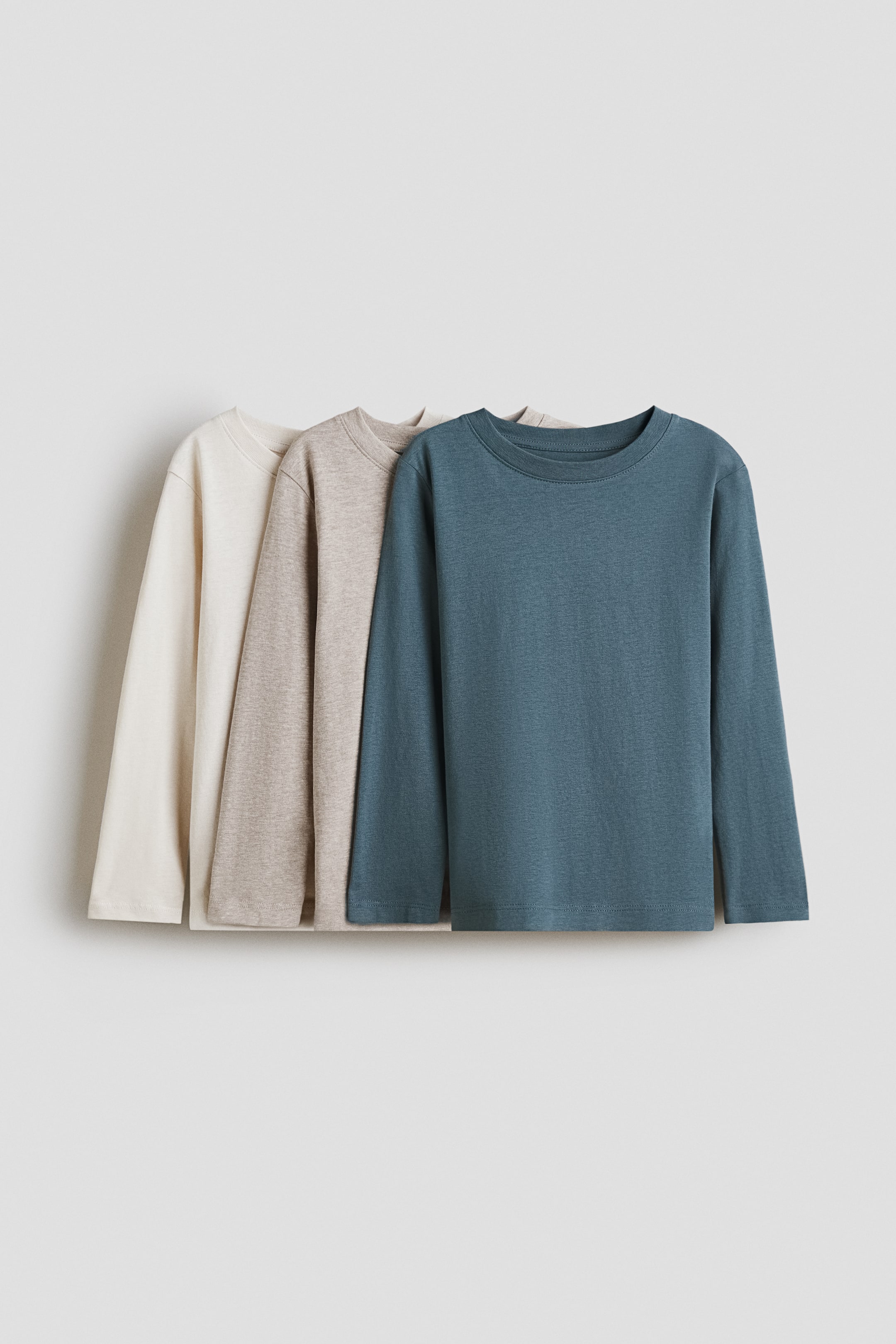 View larger image: Three long-sleeved tops are displayed front-facing, layered from back to front. Each top is made from a soft jersey fabric and features a round neckline with a narrow trim and long sleeves, in light beige, heather brown, and teal.