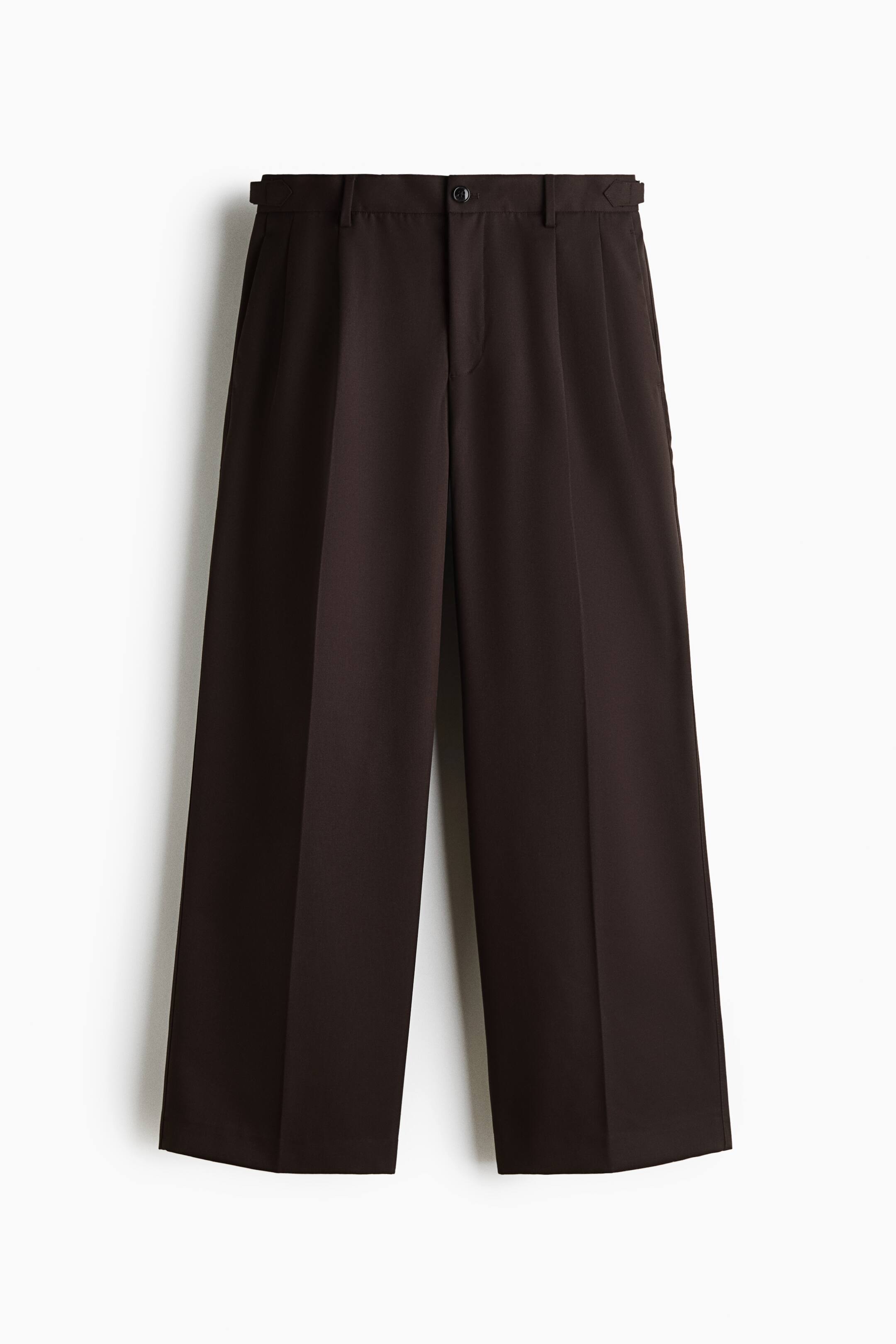 View larger image: These dark brown wide-leg trousers are hanging front-facing, featuring sharp centre creases down each leg and single front pleats. The waistband shows belt loops, a central button closure, and adjustable side tabs.