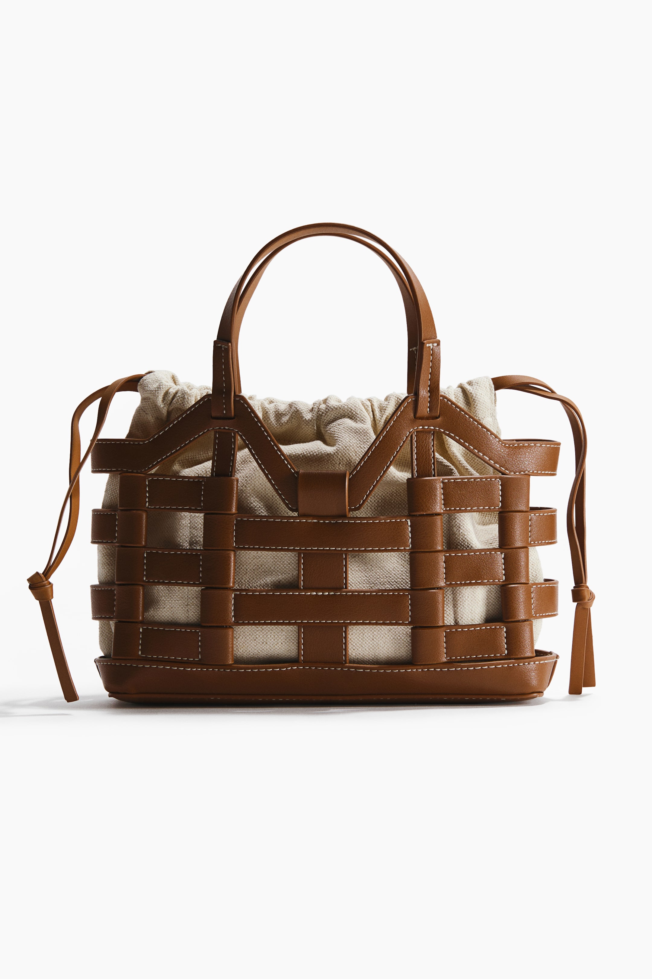 View larger image: A tote bag is shown from the front, showcasing a basket-weave exterior with brown straps and visible white stitching. A light-coloured fabric drawstring pouch serves as the inner lining, with two brown top handles arching upwards.