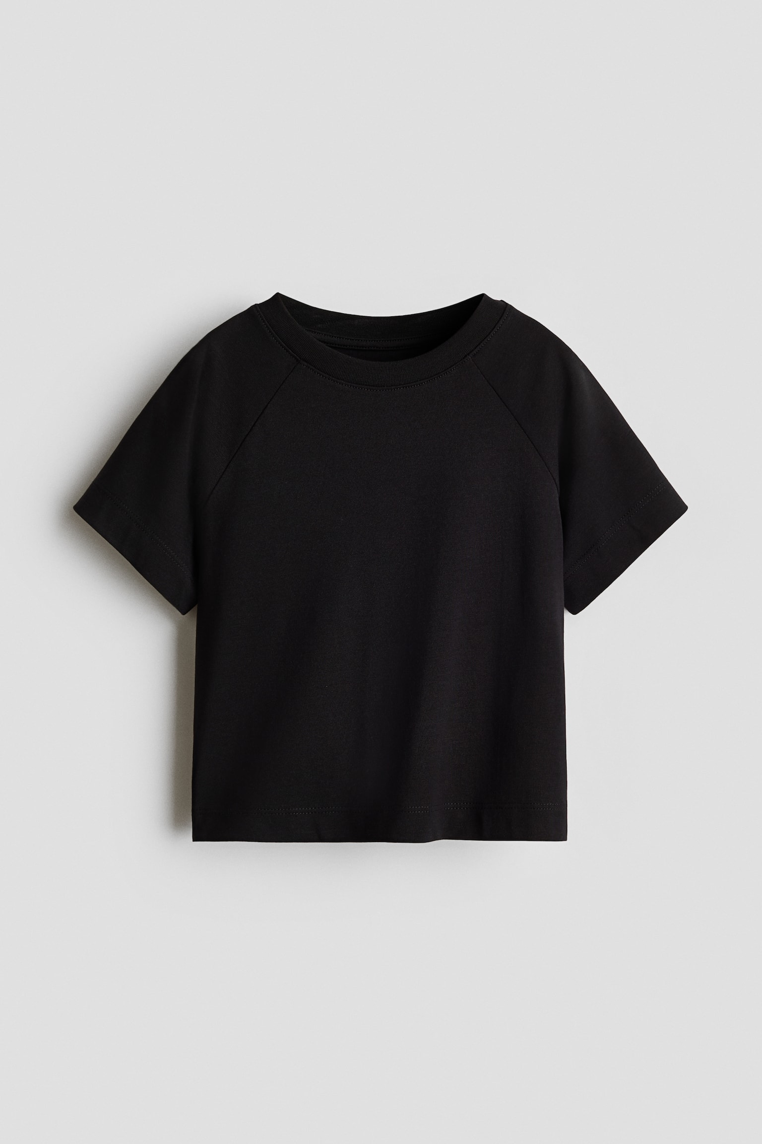 A black short-sleeved T-shirt is shown from the front, featuring a ribbed crew neckline and raglan sleeves. The T-shirt has a slightly cropped, boxy fit with clean, stitched hems at the sleeve openings and bottom hem.