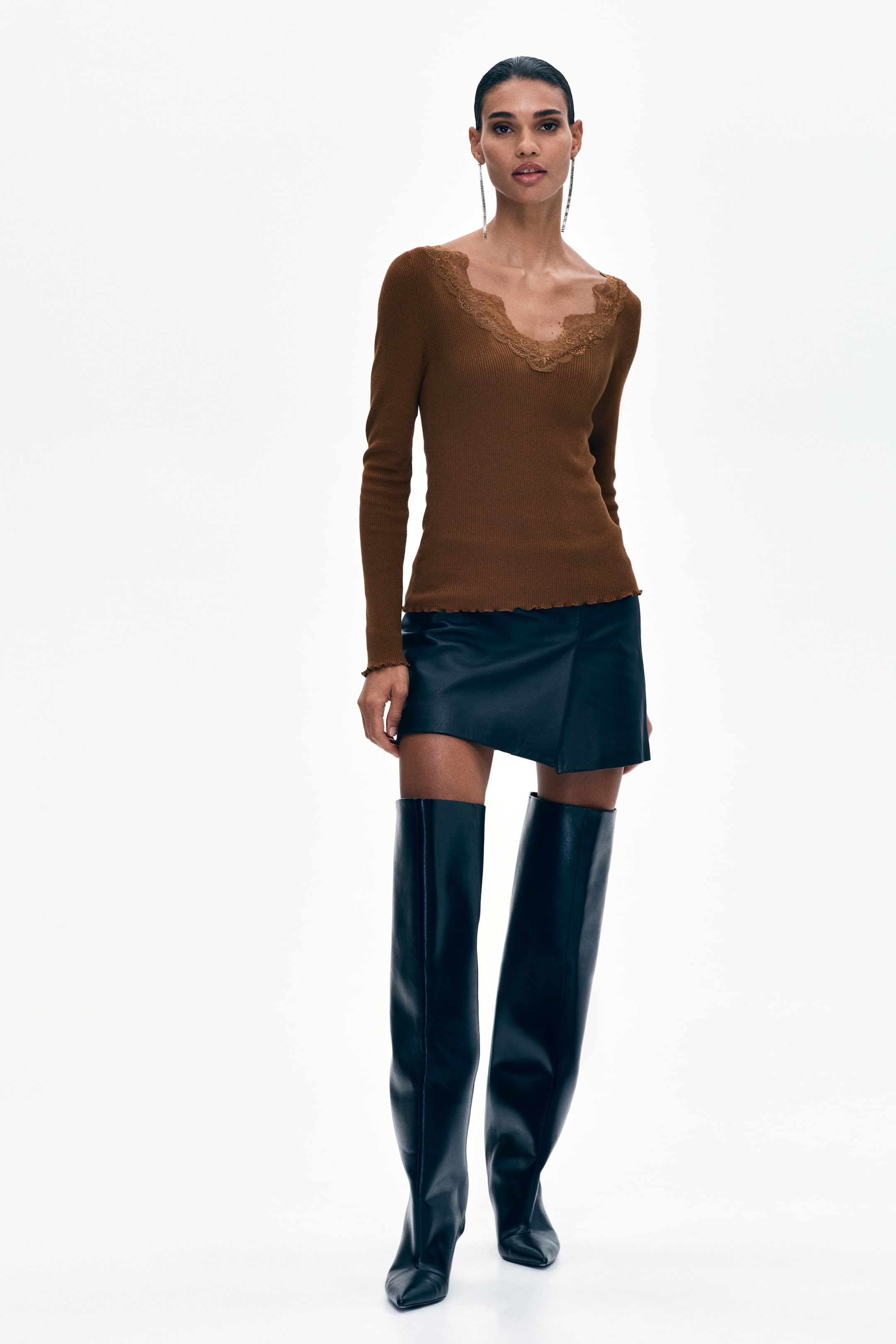 View larger image: The product showcases a brown ribbed knit long-sleeve top with a lace-trimmed V-neckline and lettuce-edge cuffs and hem. It is paired with a black faux leather mini-skirt featuring an asymmetric, lettuce-edge hem and black pointed-toe over-the-knee boots.