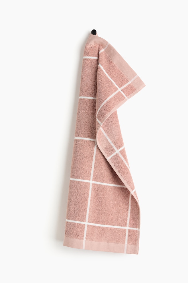 The pink terry cloth towel features a white grid pattern across its textured surface. It is hanging, with one section folded over, revealing its underside and finished edges. - 1