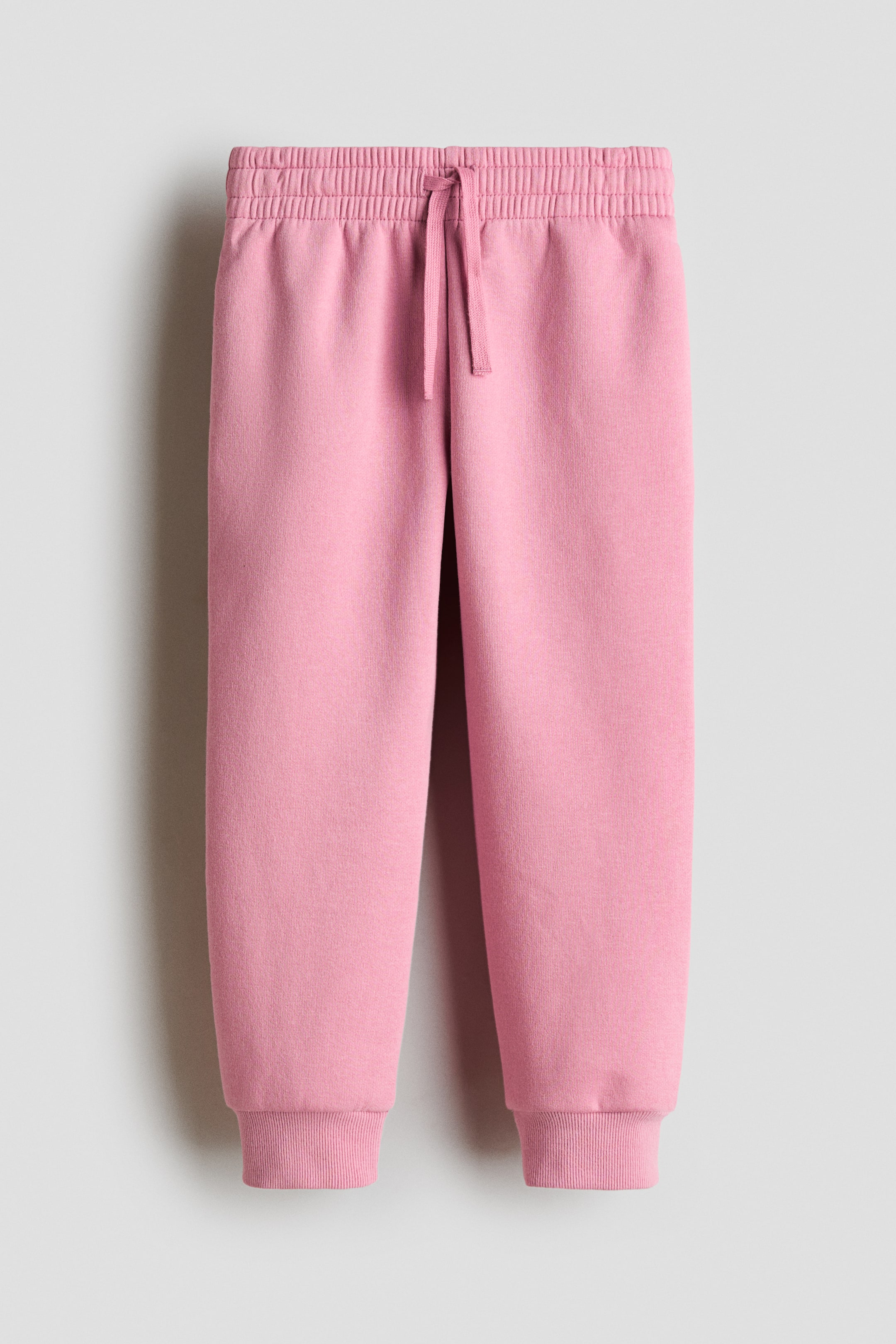 Ampliar la imagen: Los pantalones de chándal rosas se muestran desde el frente, con una pretina elástica con cordón ajustable y puños acanalados.