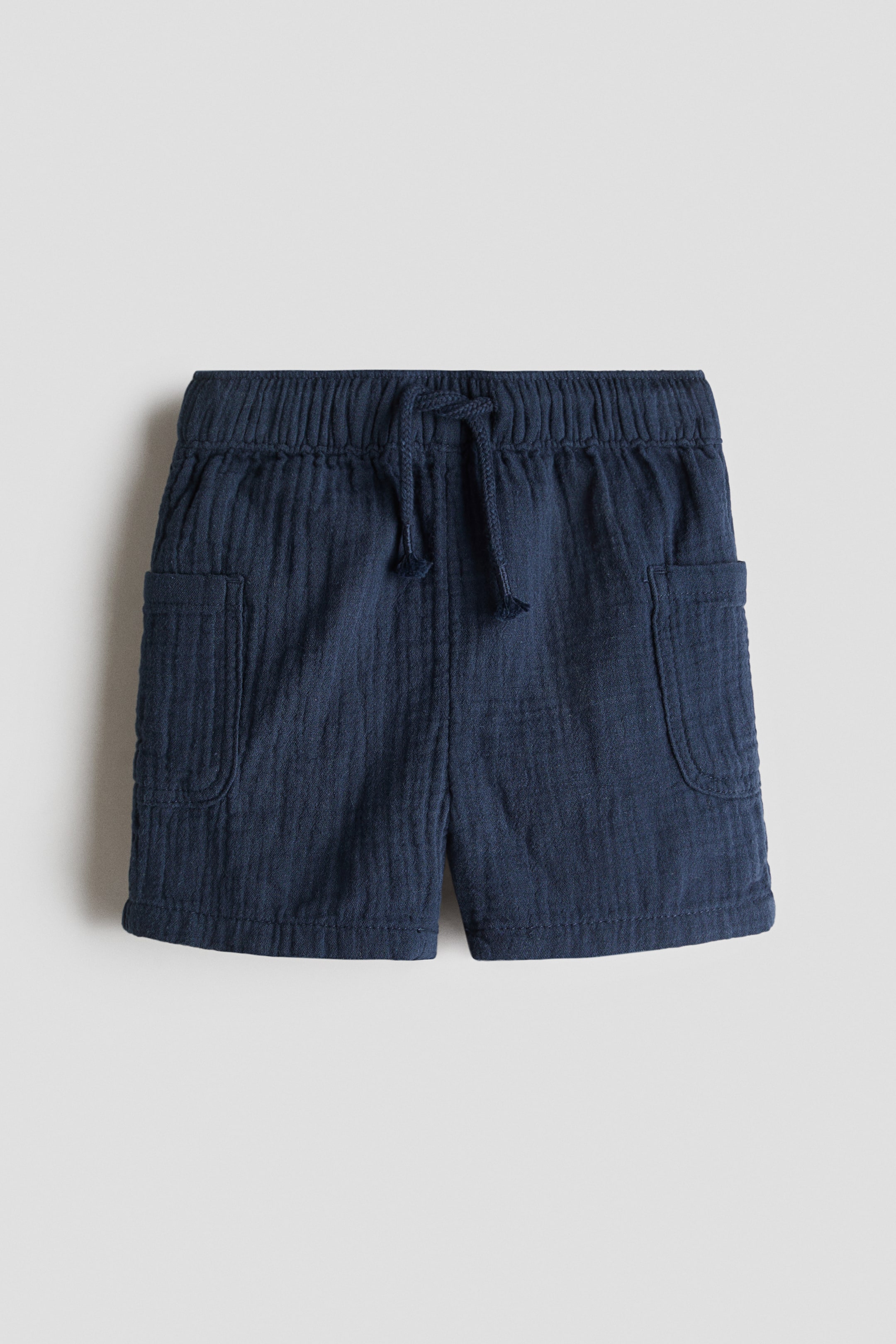 View larger image: Navy blue shorts feature a textured fabric, an elastic waistband with a tied drawstring, and two front patch pockets.