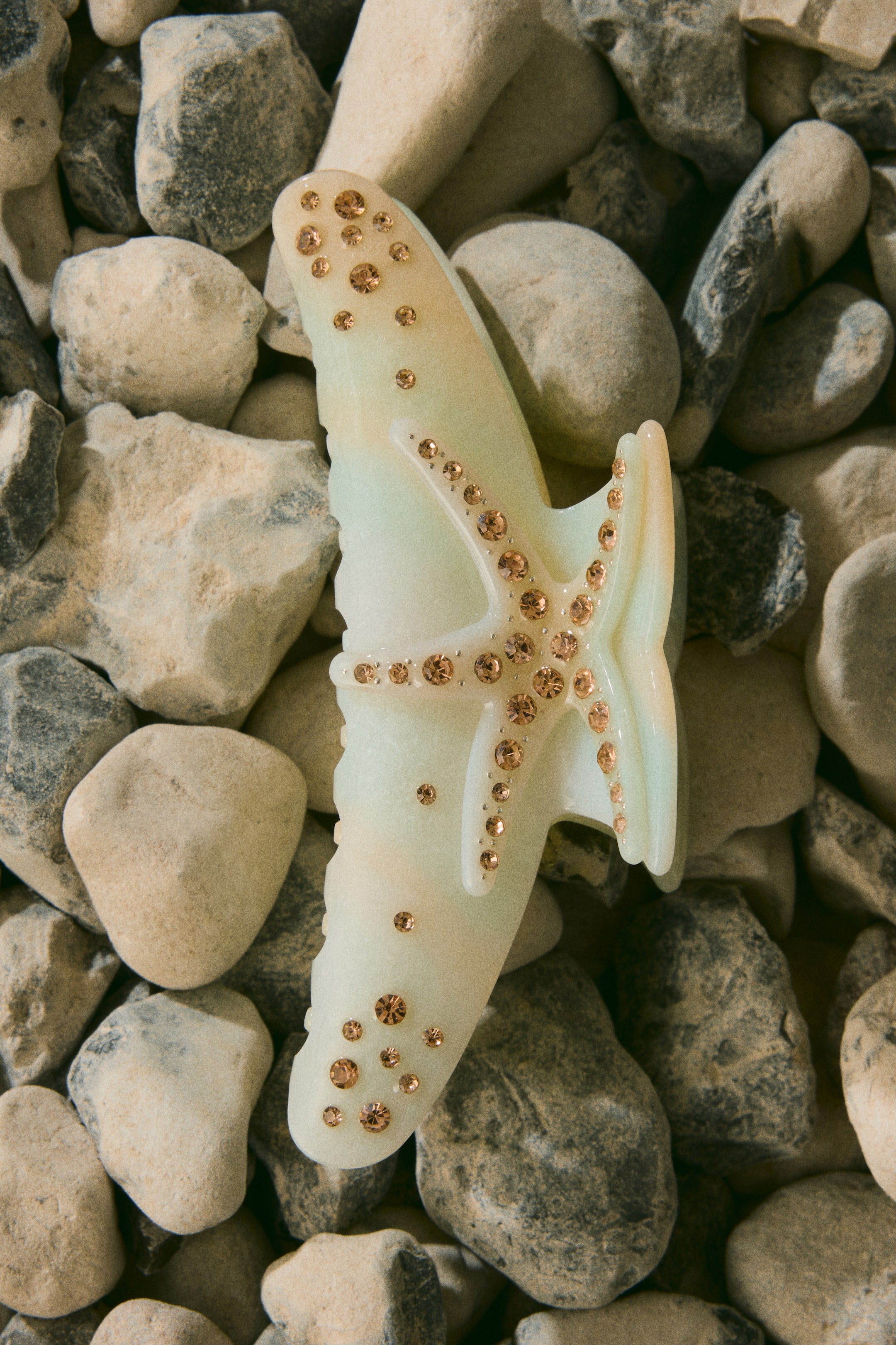 View larger image: A translucent, marbled pale green hair claw clip, shaped like a stylized shark or marine creature, is lying flat and facing upwards. It features numerous small, light brown rhinestones arranged in a starfish pattern on its central body and scattered across its front and rear sections.