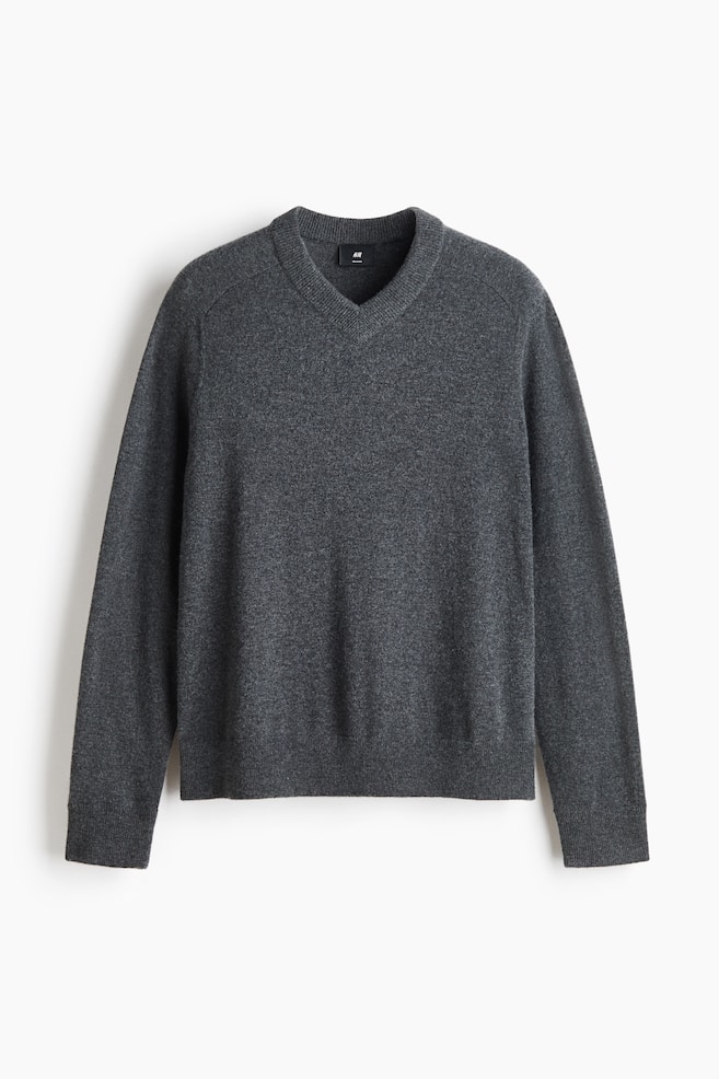 Un maglione in maglia grigio scuro Ã¨ mostrato frontalmente, con scollo a V a coste, maniche lunghe con polsini a coste e orlo a coste. Il maglione presenta una texture morbida e a maglia fine con dettagli di cuciture diagonali vicino alle spalle. - 1