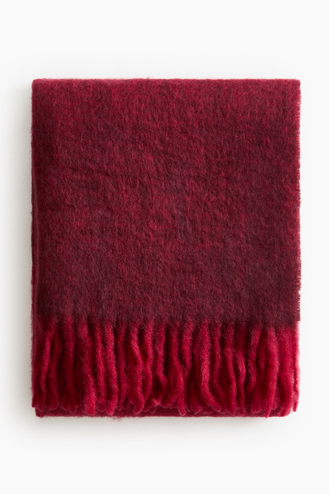 Una manta de color rojo intenso está doblada en forma de rectángulo, presentando una textura suave y esponjosa y un fleco rojo brillante a lo largo de su borde inferior. - 1