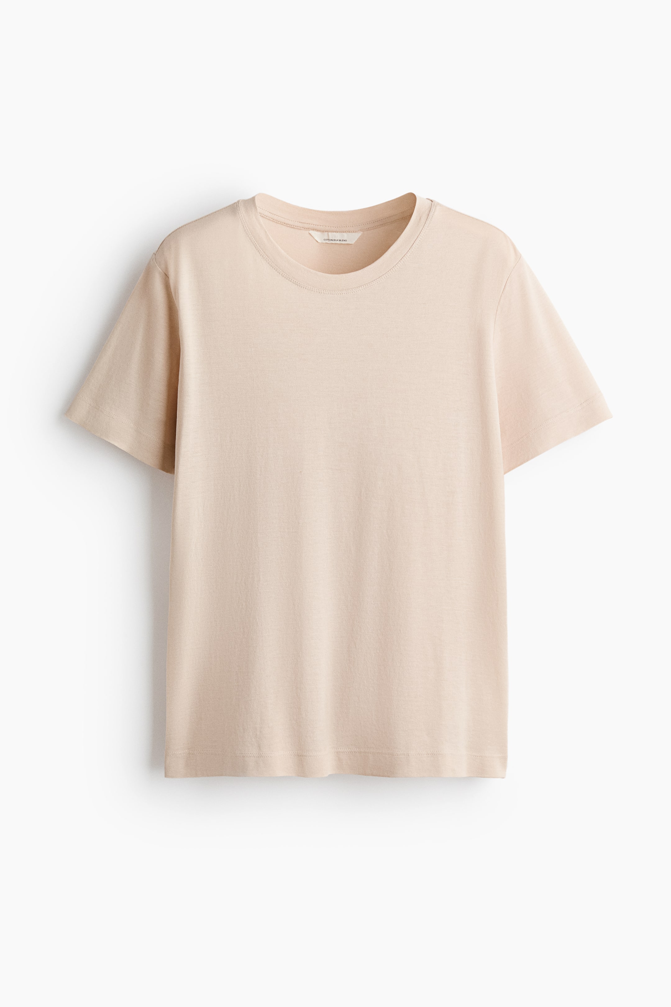 Visualizza immagine più grande: Una t-shirt beige chiaro è presentata nella sua vista frontale, caratterizzata da un collo rotondo e maniche corte. Il tessuto appare morbido e cade delicatamente.