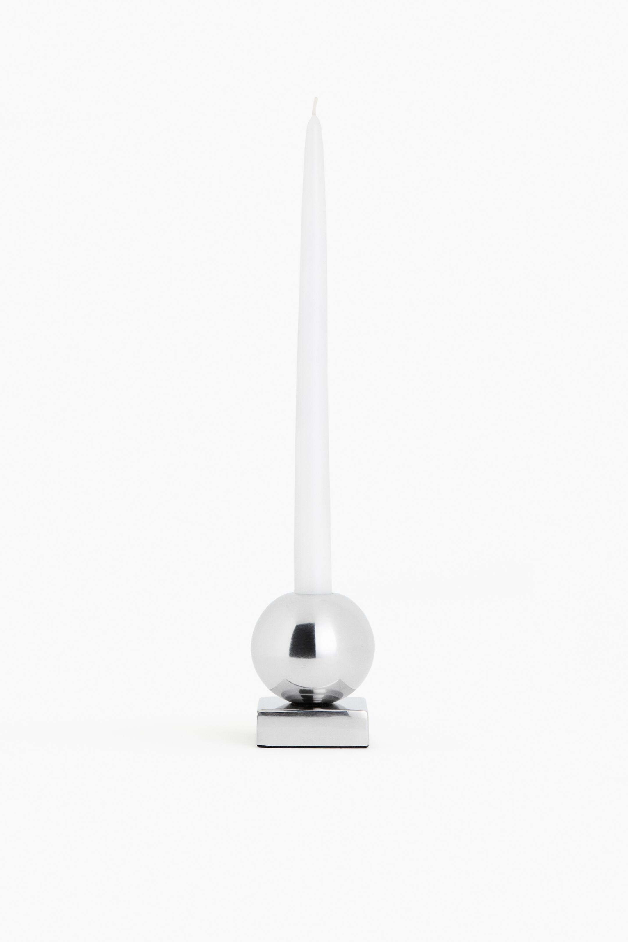 View larger image: A polished metallic silver candle holder is shown facing front, featuring a square base supporting a spherical body. A tall white taper candle stands upright, extending from the top of the spherical holder.